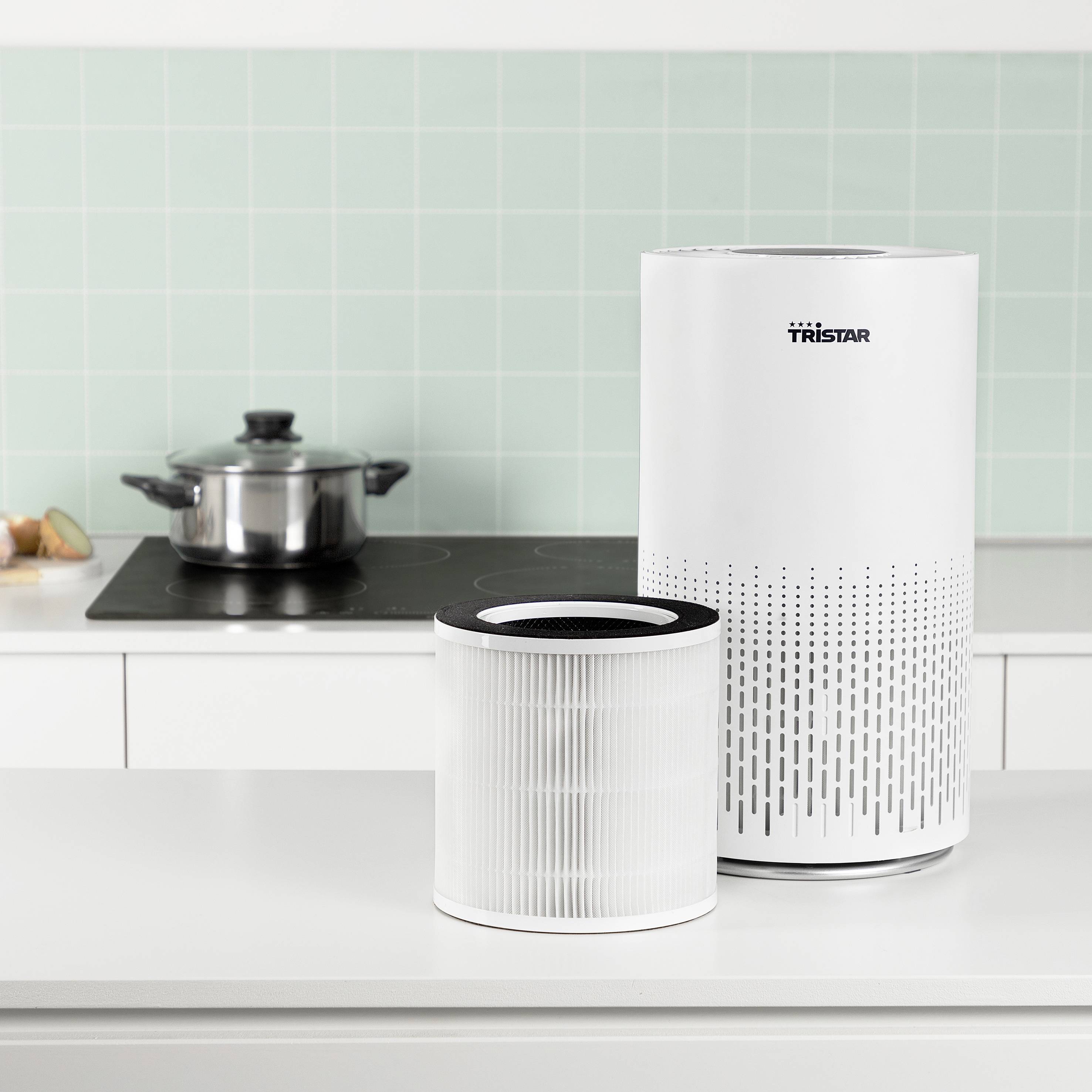 Luchtreiniger en filters op een keukentoonbank met een pan op een fornuis op de achtergrond.