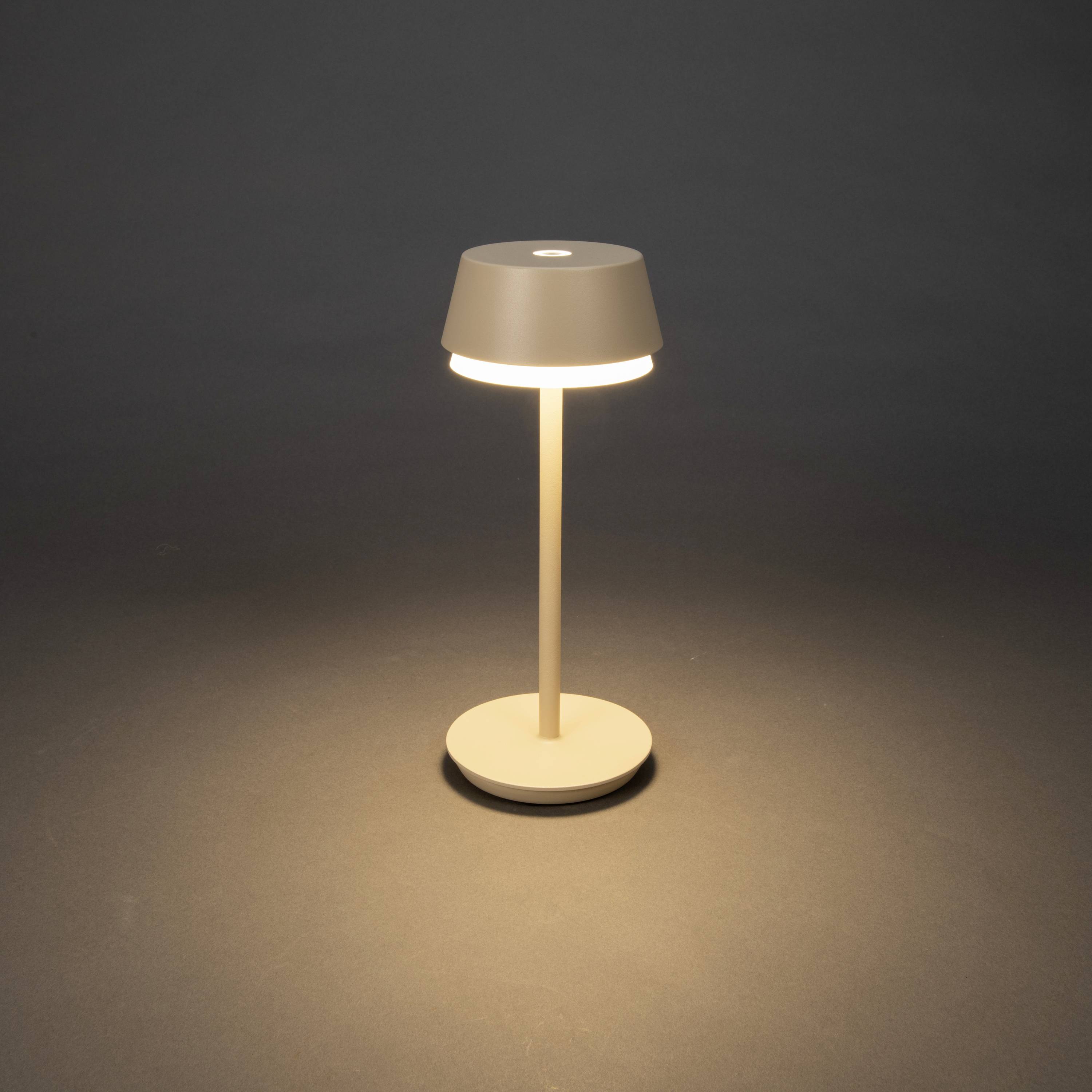 Een slanke tafellamp met een ronde kap verlicht een verder donkere ruimte en creëert een warme lichtgloed op de vloer.