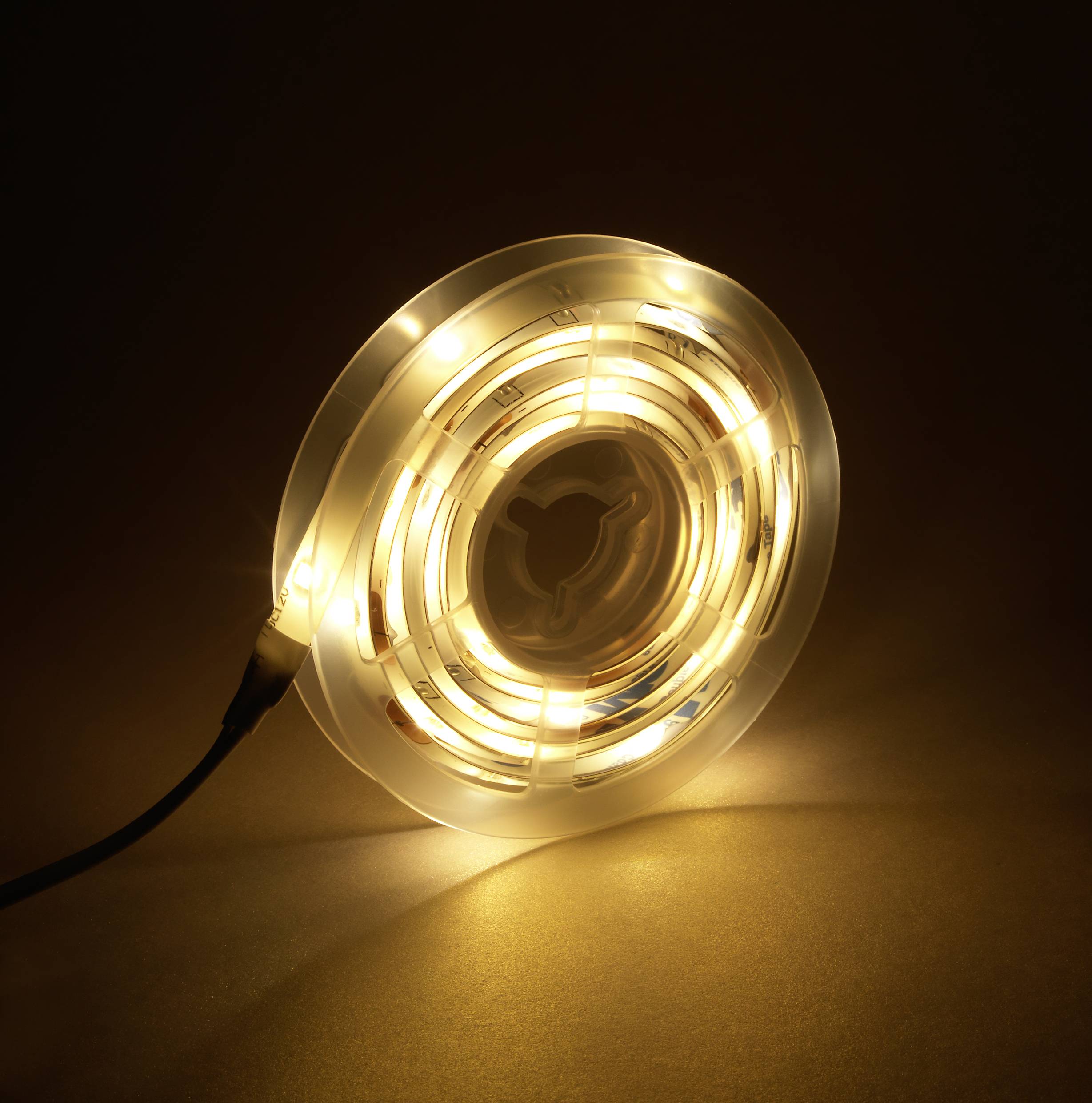 Een opgerolde LED-lichtslinger straalt warm, geel licht uit en ligt op een donkere achtergrond.