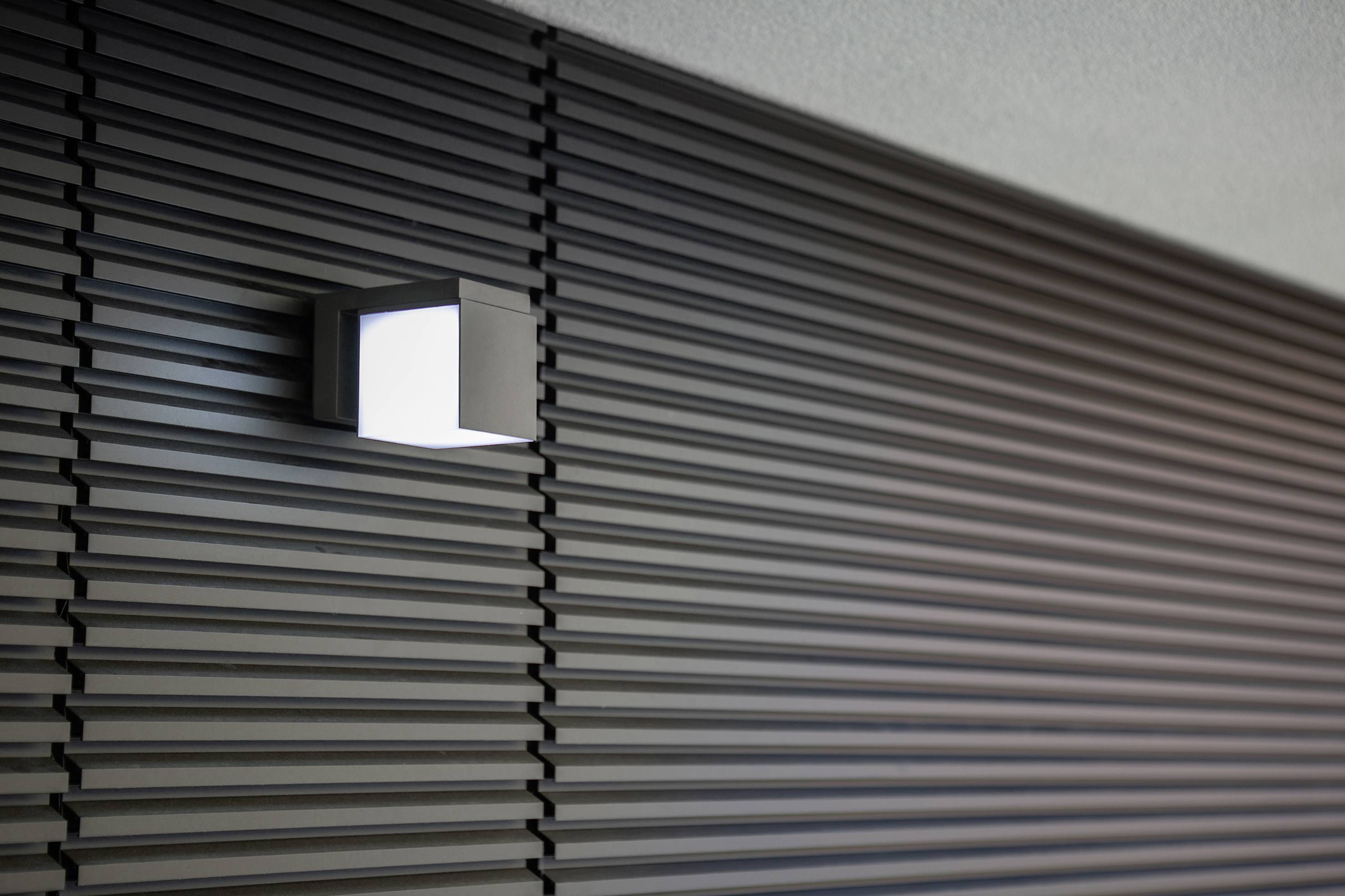Muur met moderne kubusverlichting die licht uitstraalt naar boven en beneden. Achtergrond van horizontale, zwarte lamellen.