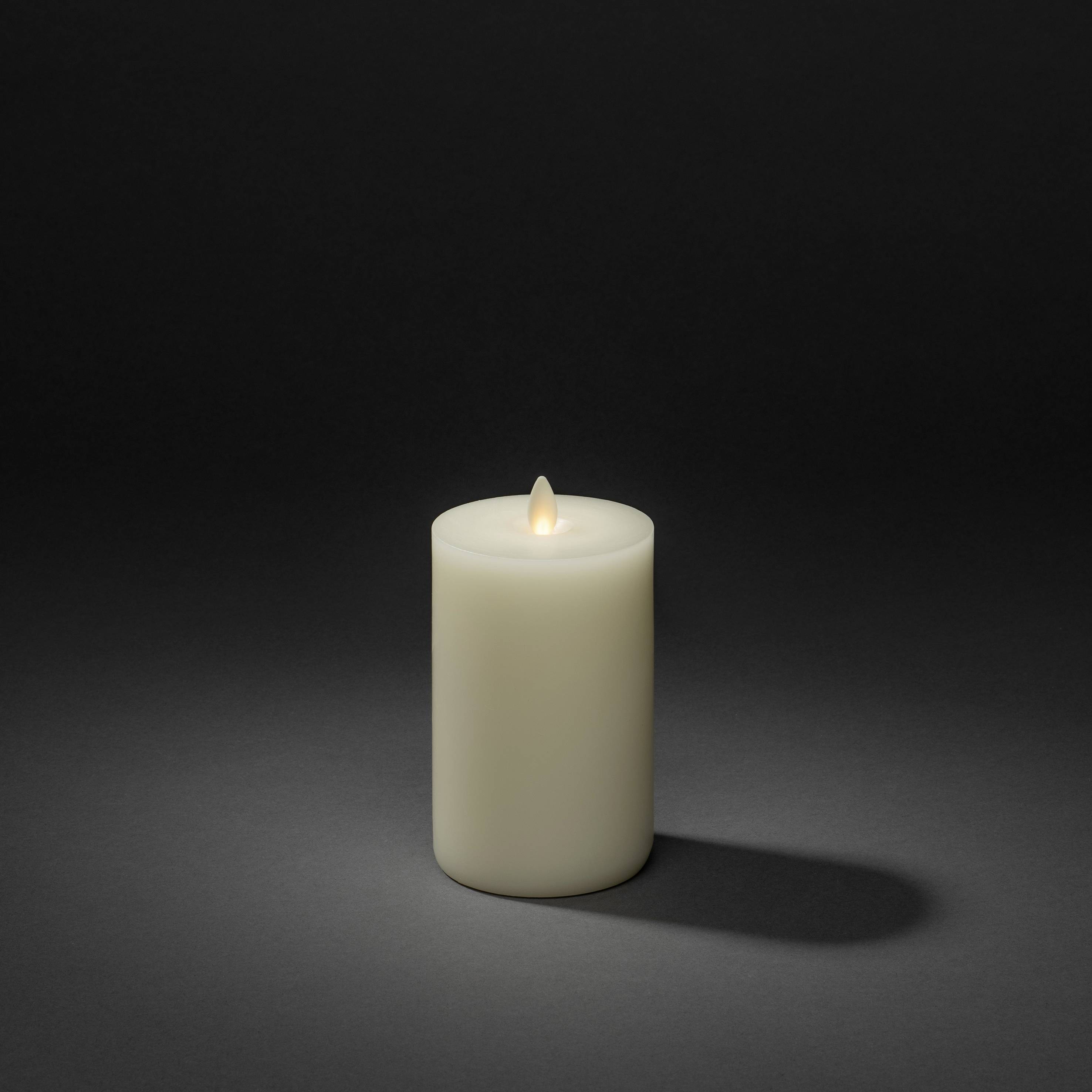 Witte kaars voor een donkergrijze achtergrond met een kleine vlam aan de bovenkant.