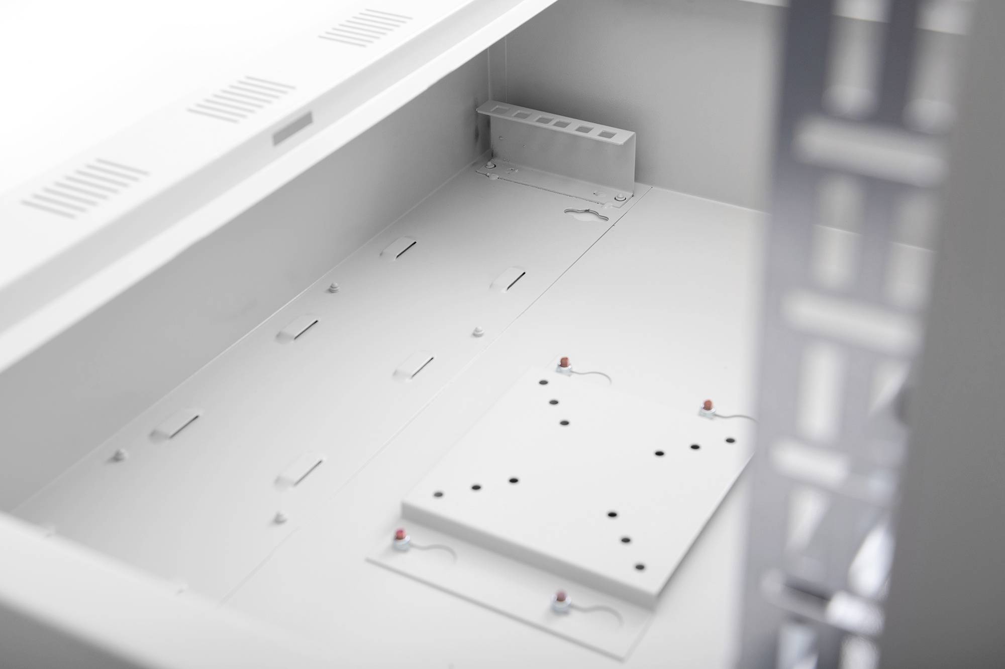 Een leeg, wit computerbehuizing-interieur met bevestigingsbeugels en ventilatierooster zichtbaar, klaar voor de installatie van hardwarecomponenten.