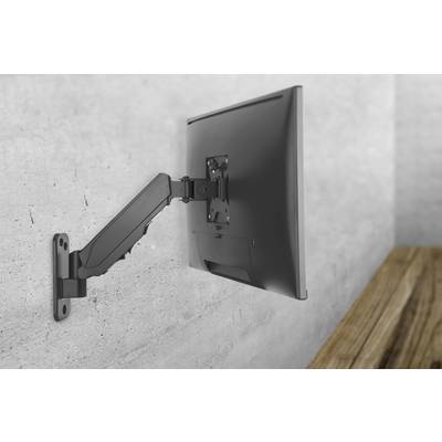 Een zwarte computermonitor is gemonteerd aan een beweegbare arm tegen een grijze muur. Naast de monitor staat een houten bureau.