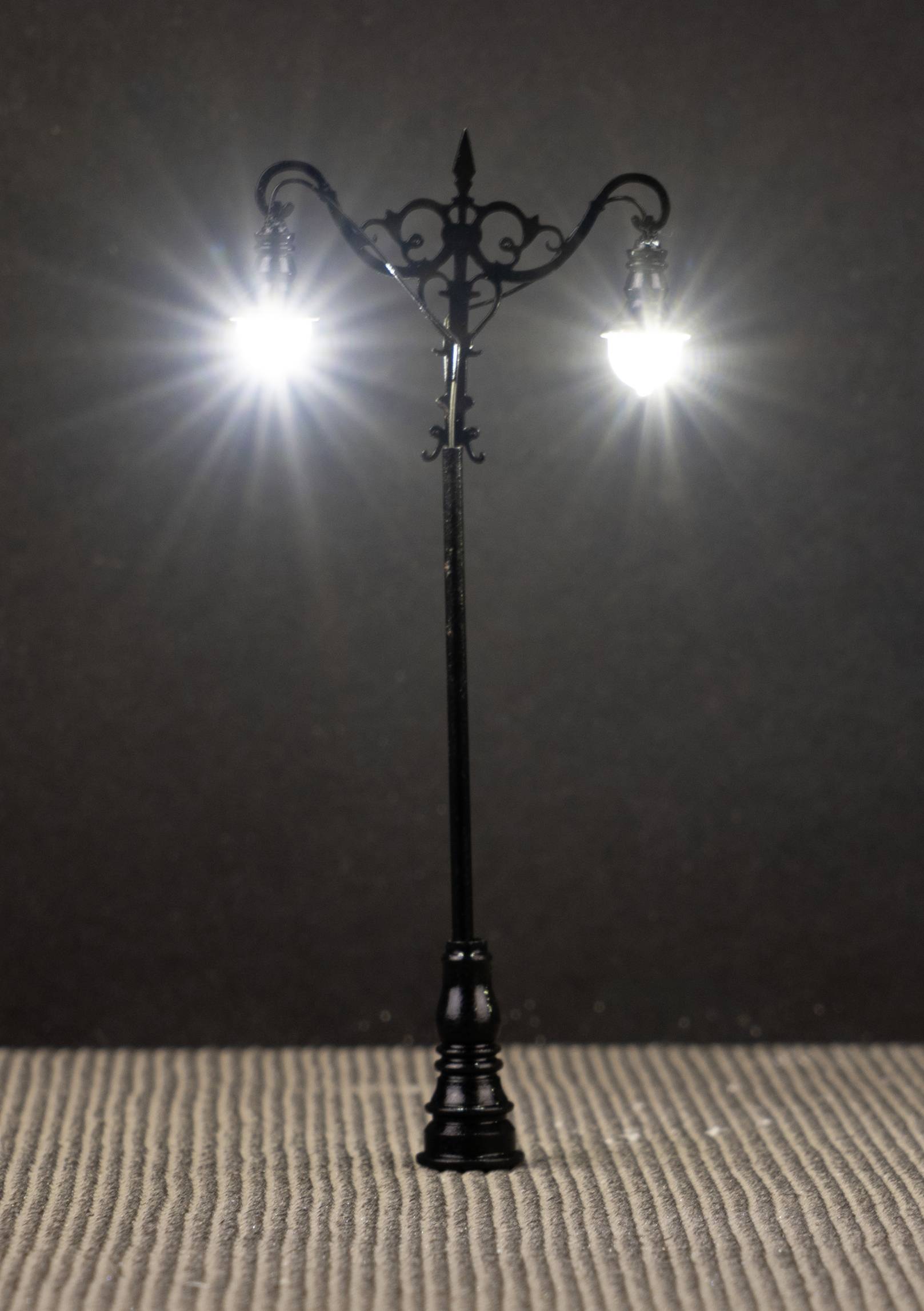 Een decoratieve, antieke straatlantaarn met twee brandende lampen op een gestructureerde ondergrond.