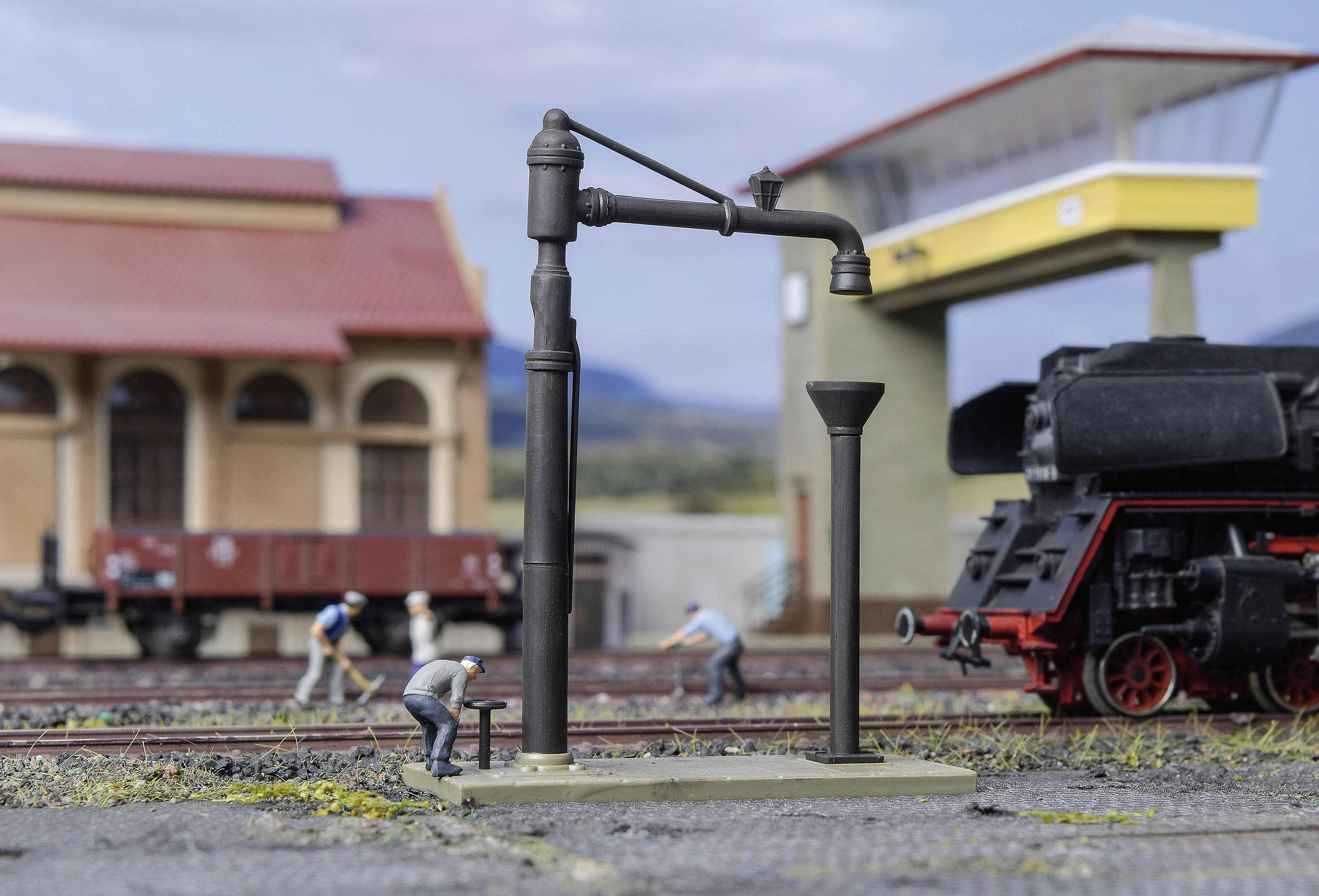 Verschillende personen werken aan een modelspoorbaan met een watertoren en een stoomlocomotief op de voorgrond.