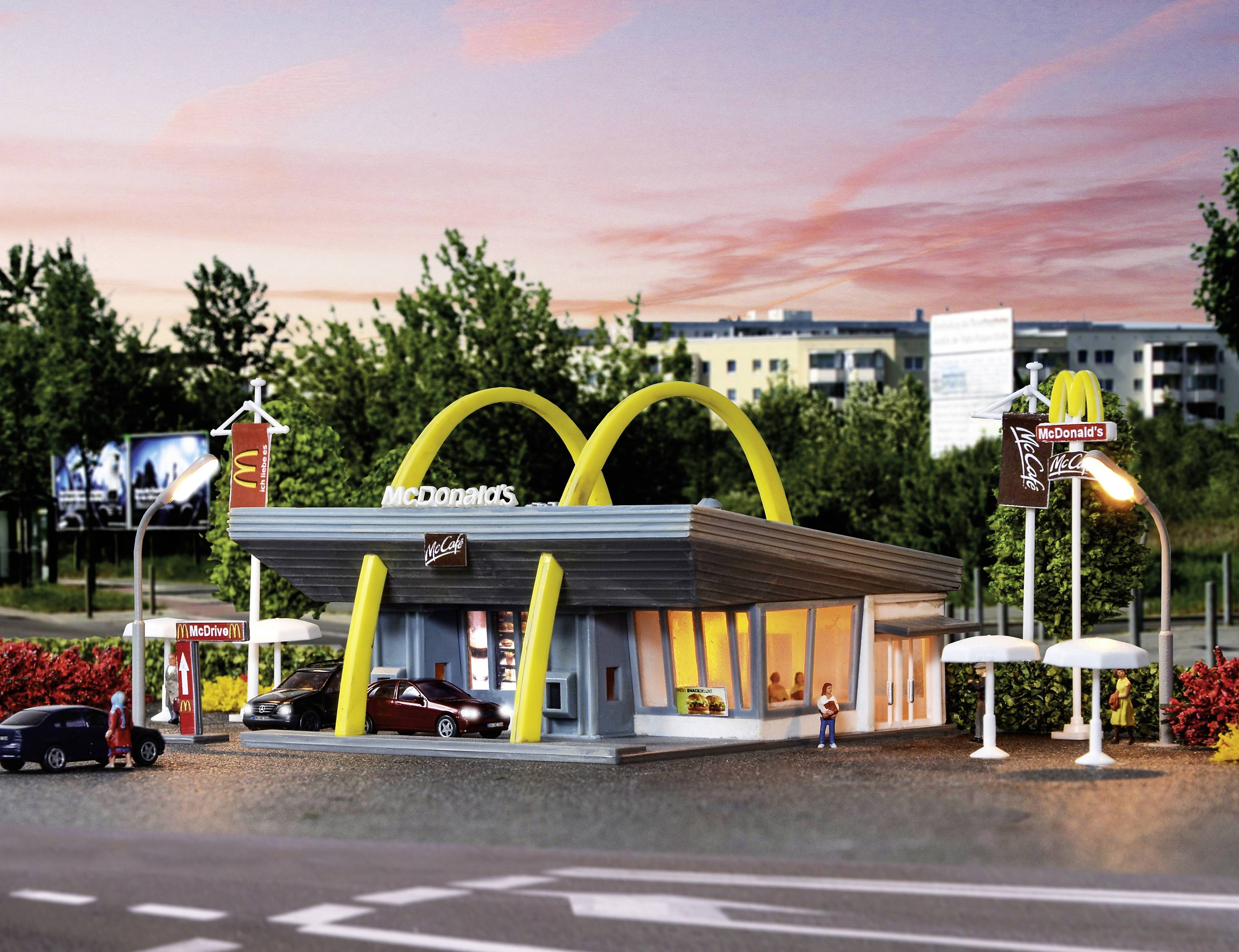 Een miniatuurmodel van een McDonald's-restaurant met opvallende gele bogen, auto's ervoor geparkeerd. Op de achtergrond zijn bomen en gebouwen te zien.