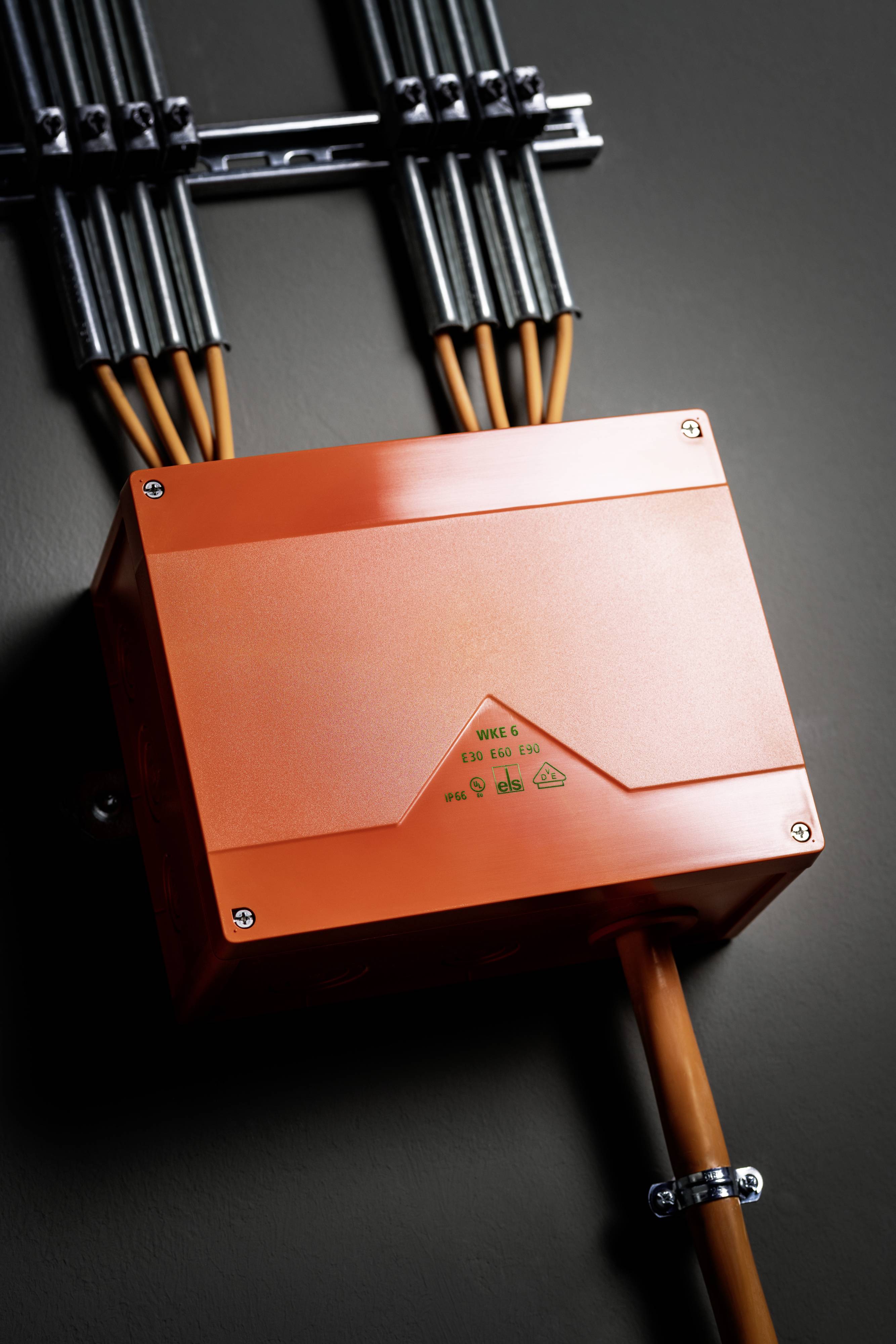 Een oranje elektrische verdeeldoos met kabels op meerdere aansluitingen, gemonteerd aan een donkere muur.