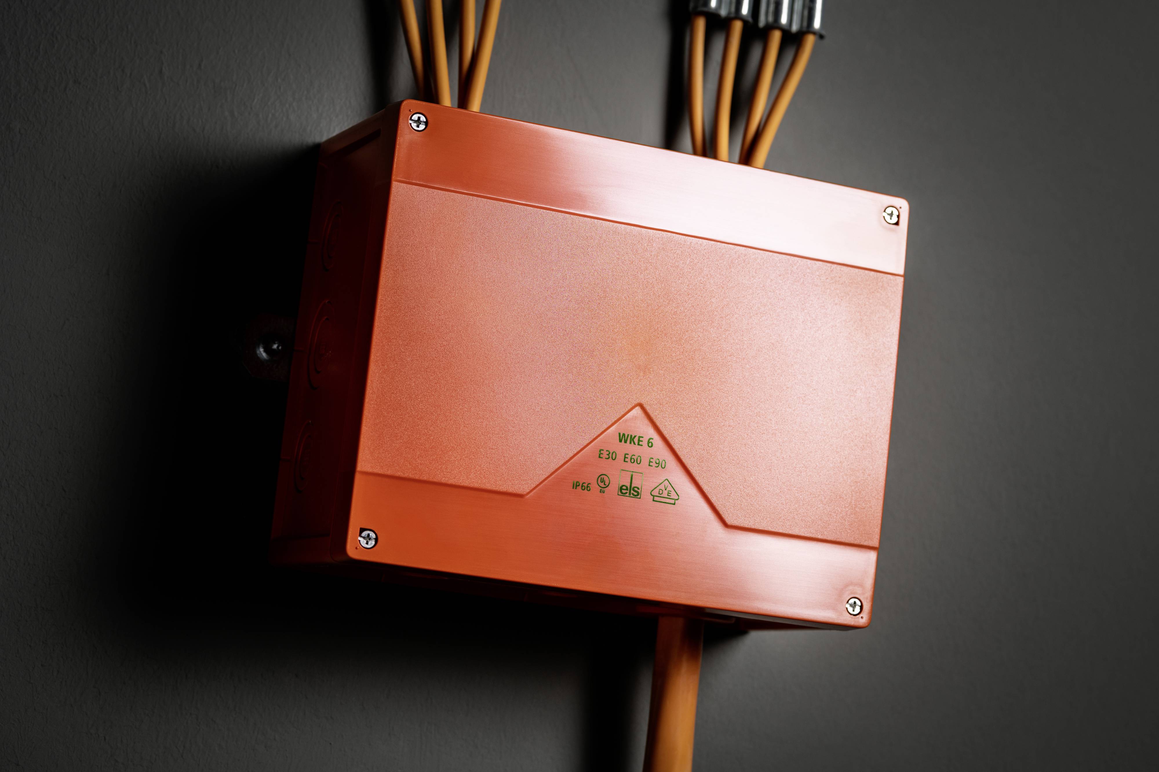 Een oranje controledoos aan een grijze muur met meerdere kabels die van boven en beneden zijn aangesloten.