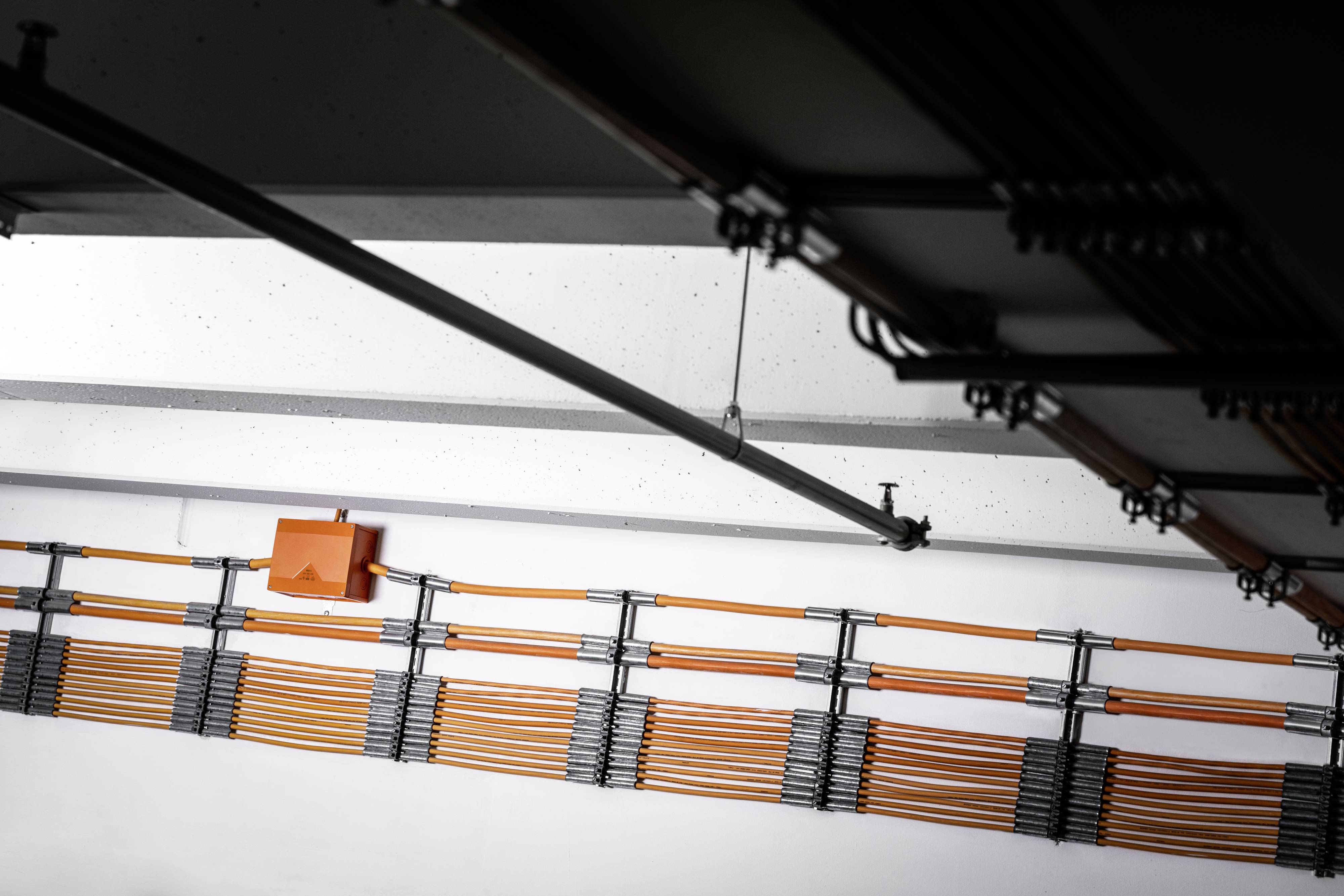 Kabelbeheer aan een plafond: Oranje kabels, bevestigd aan metalen dragers, lopen parallel en netjes georganiseerd.