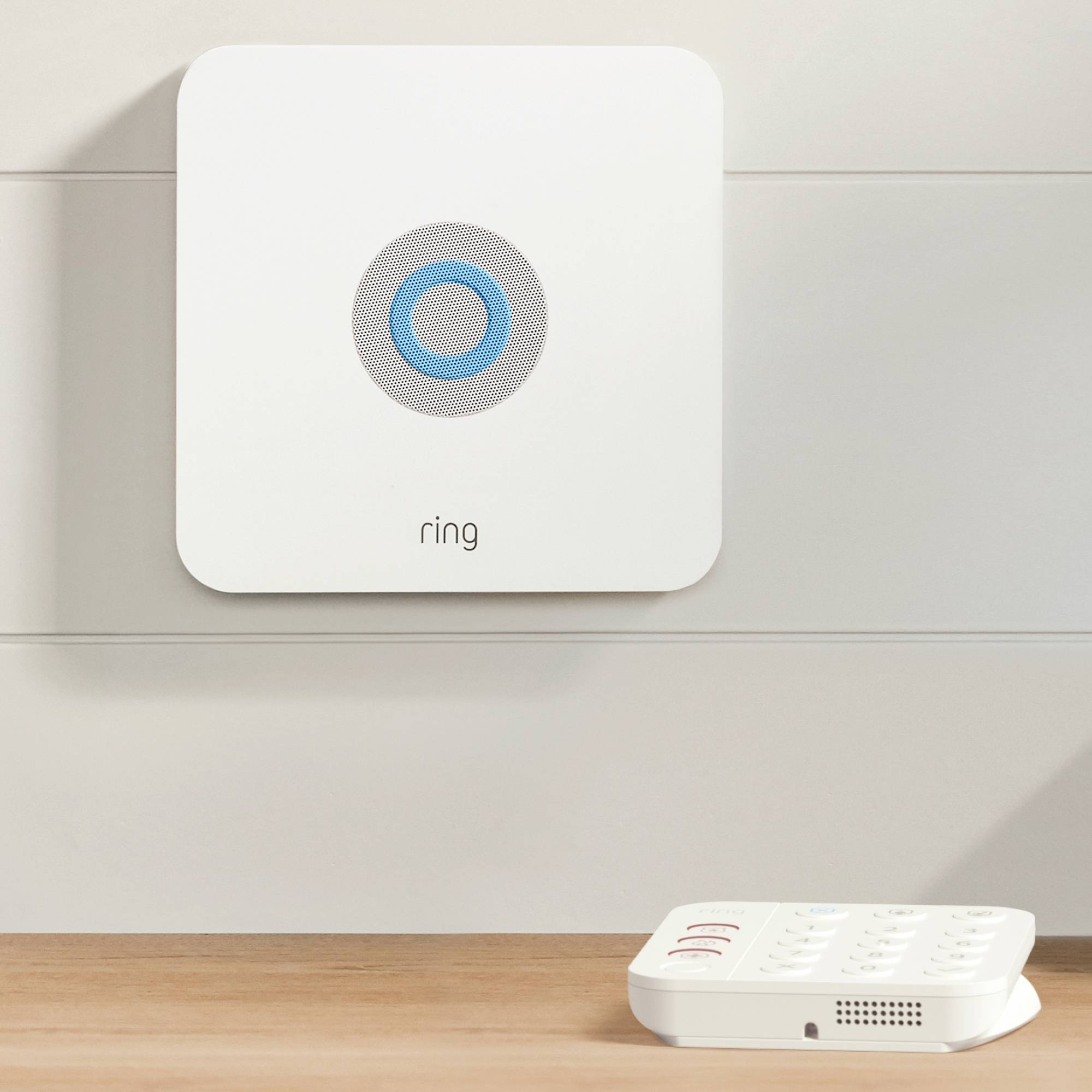 Een wit apparaat met een blauwe ring in het midden en de tekst 'ring' eronder op een muur, naast een wit bedieningspaneel.