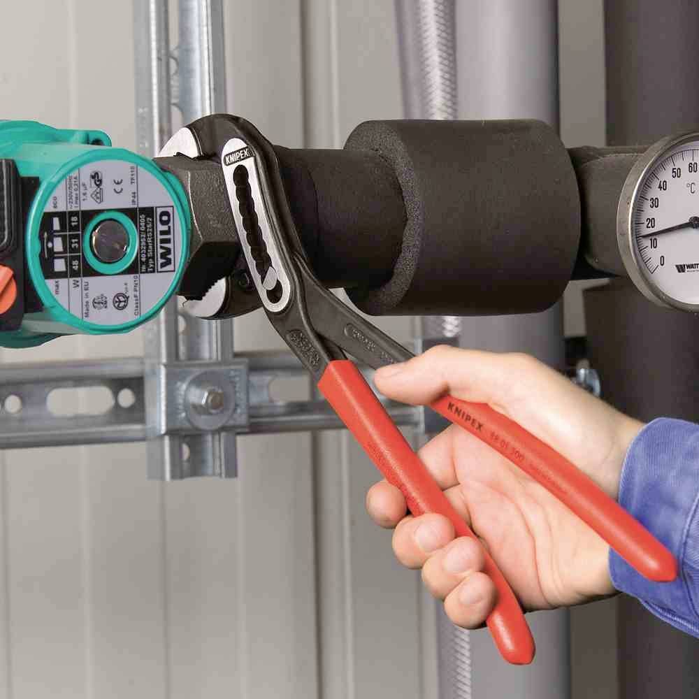 Een persoon draait een verbinding aan op een zwart buizensysteem met een meetinstrument, gebruikmakend van een rode pijptang.