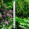 Een thermometer toont 25°C in een tuin met roze bloeiende planten en groen gebladerte op de achtergrond.