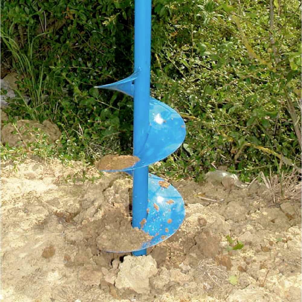 Een blauwe aardboormachine graaft een gat in zanderige grond, omringd door groene vegetatie op de achtergrond.