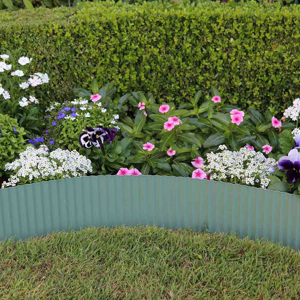 Een kleurrijk bloemenperk met bloemen in verschillende tinten, omrand door een groene metalen rand en omgeven door netjes gemaaid gazon.