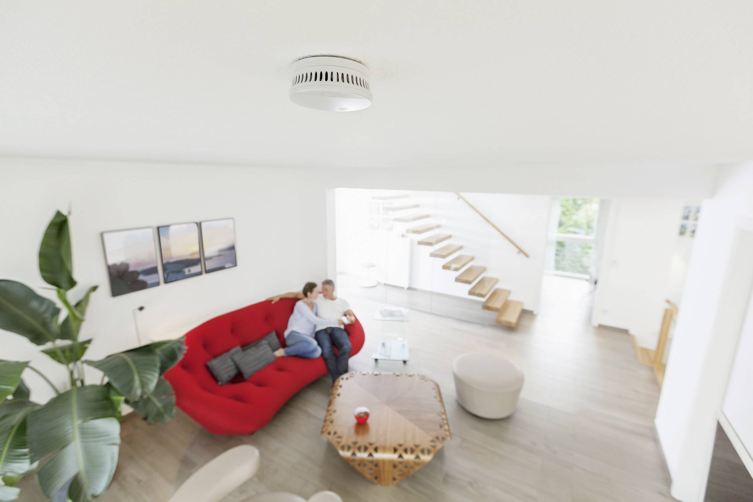 Een stel zit ontspannen op een rode bank in een moderne woonkamer. Op een tafel in het midden staat een rode mok.