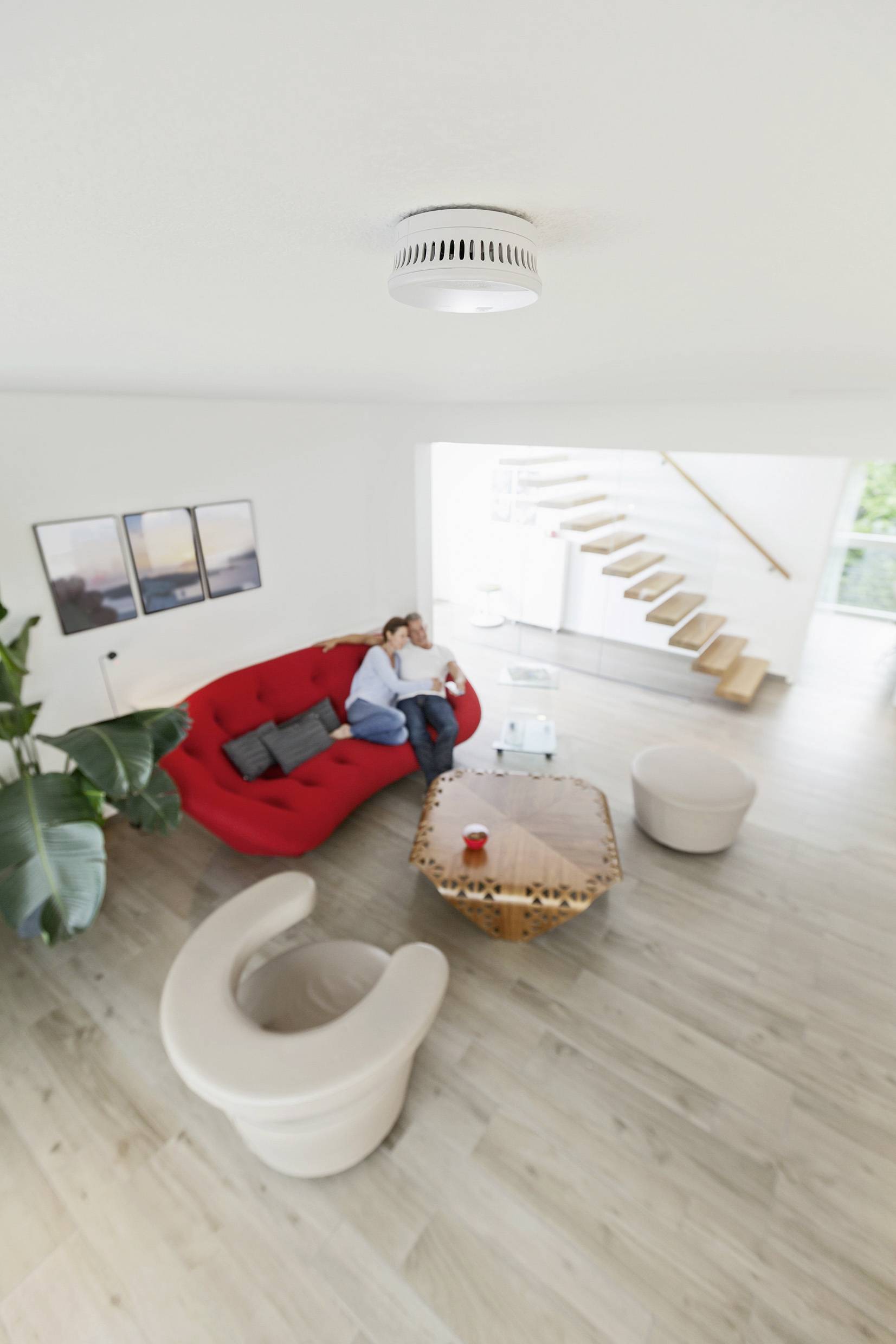 Woonkamer met rode bank, twee fauteuils en salontafel. Personen zitten op de bank. Moderne, lichte inrichting.