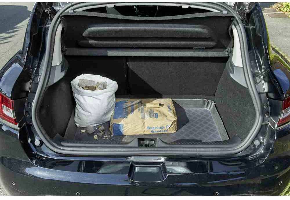 Een open kofferbak van een auto met een zak grind en een verpakking bouwmateriaal.