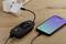 Een smartphone en een USB-vermogensmeter zijn verbonden op een houten tafel. Het display toont spanning, stroom en vermogen.