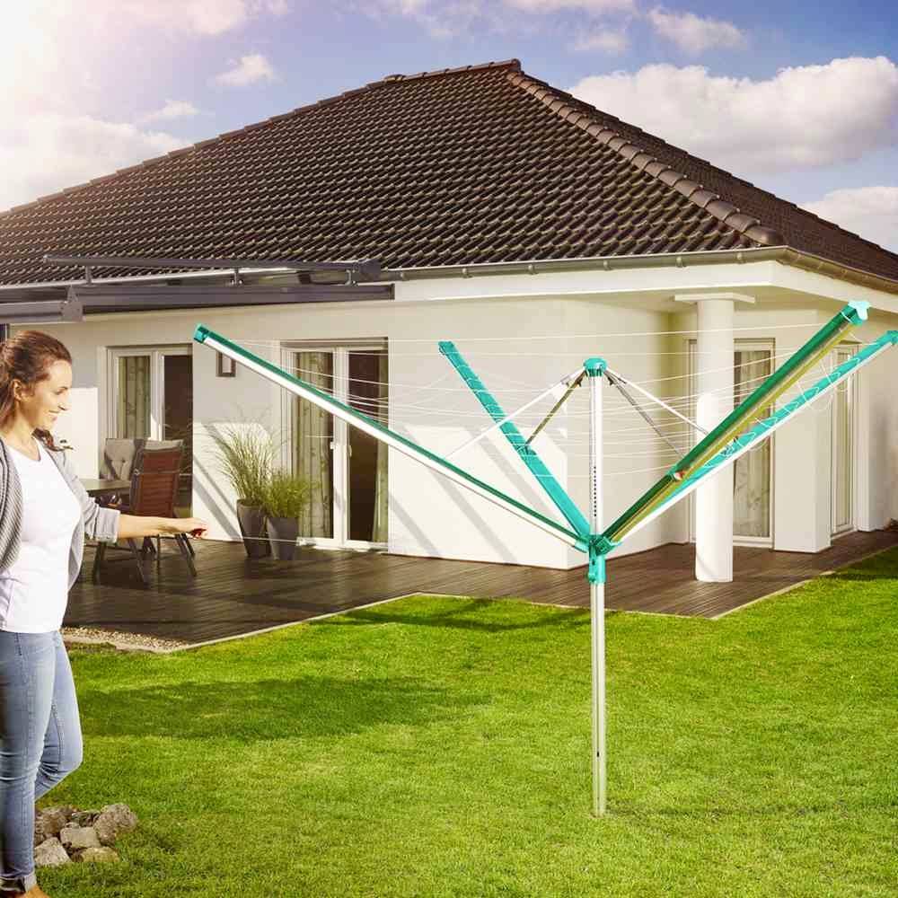 Een persoon staat in de tuin naast een opengevouwen, vrijstaande wasrek. Op de achtergrond is een modern huis te zien.
