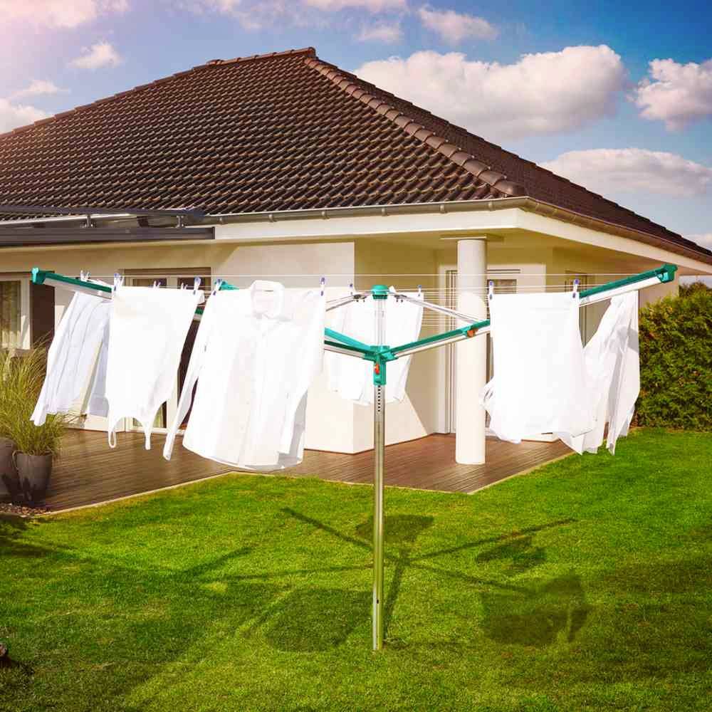 Een groene droogmolen staat in de tuin van een modern huis, behangen met witte kledingstukken onder een blauwe lucht met wolken.