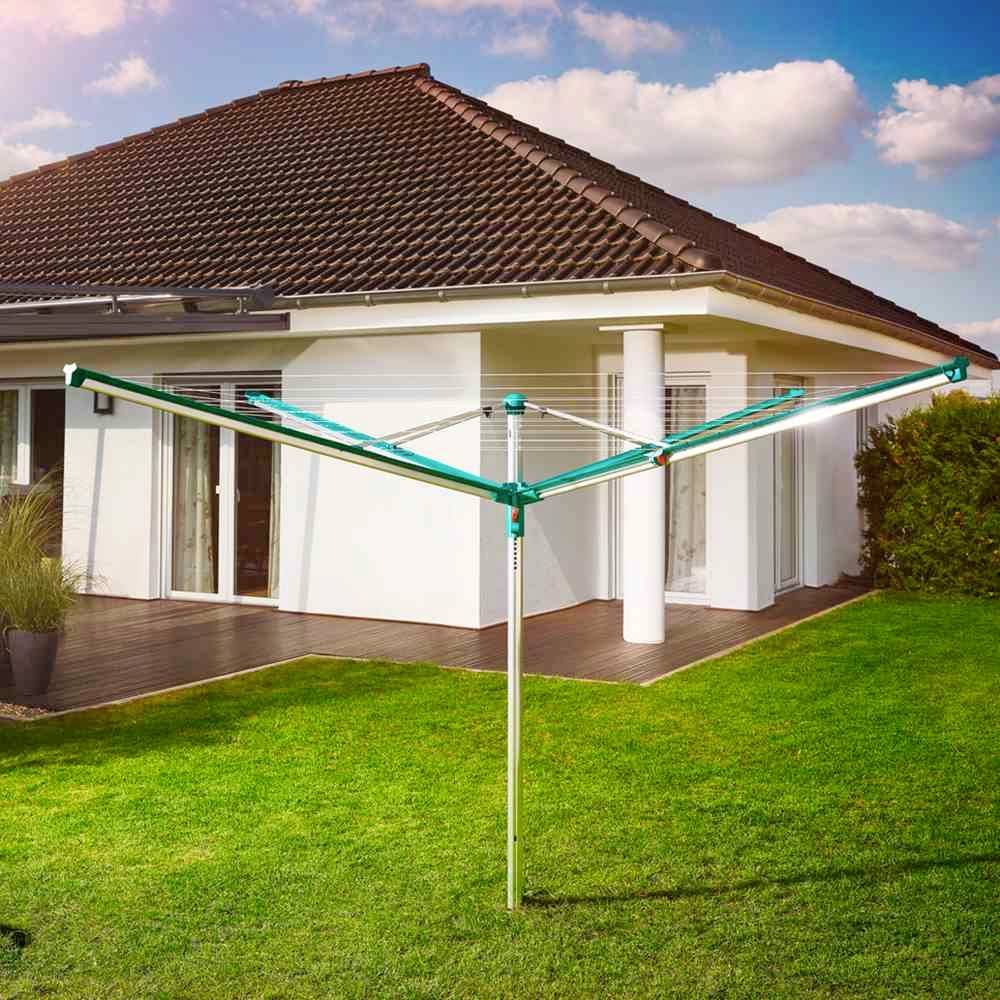 Een wasrek staat op een goed onderhouden gazon voor een modern huis met een terrasruimte, dat wordt verlicht door zonlicht.