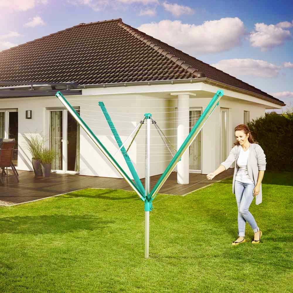 Een vrouw spant in een tuin een blauwe waslijn uit naast een huis.