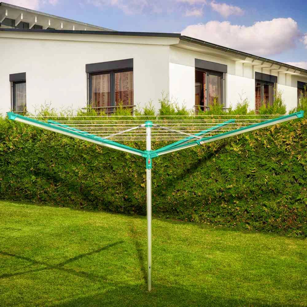 Groene droogmolen in de tuin voor een haag en een wit huis bij zonnig weer.