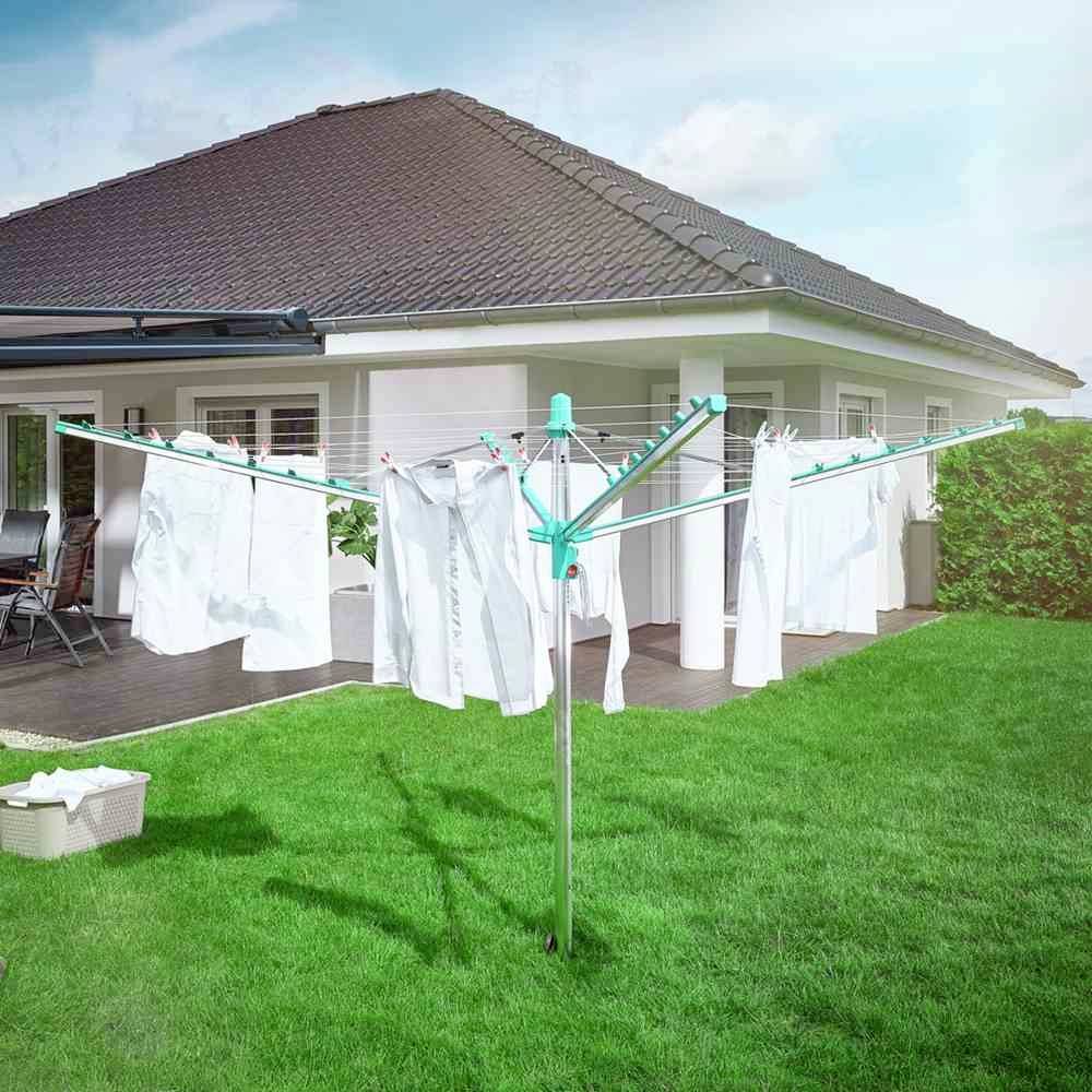 Was hangt er wasgoed te drogen op een rond droogrek in de tuin van een vrijstaande woning. Op de achtergrond is het terras zichtbaar.