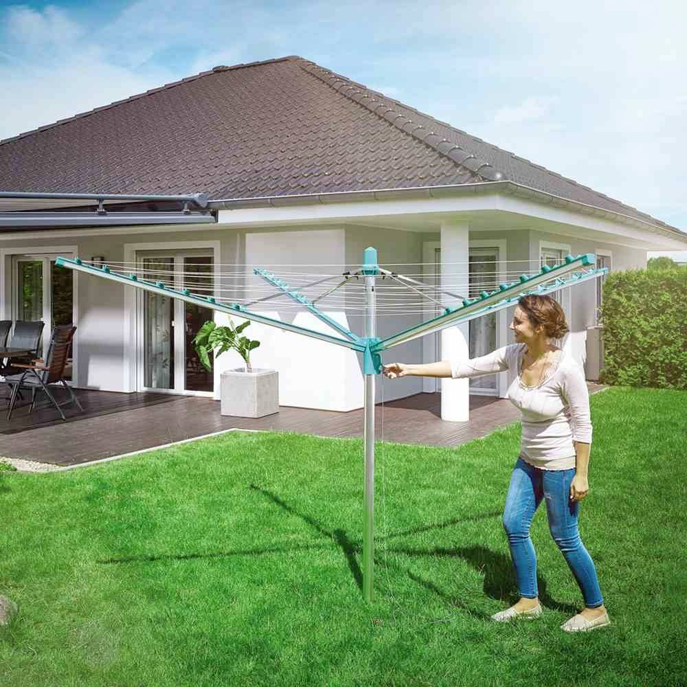Een vrouw zet een wasrek op in de tuin. Op de achtergrond is een modern vrijstaand huis met een overdekt terras te zien.