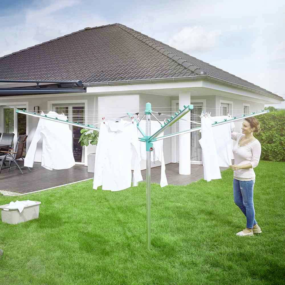 Een vrouw hangt wit wasgoed op aan een droogrek in de tuin. Op de achtergrond staat een wit huis met een grijs dak.