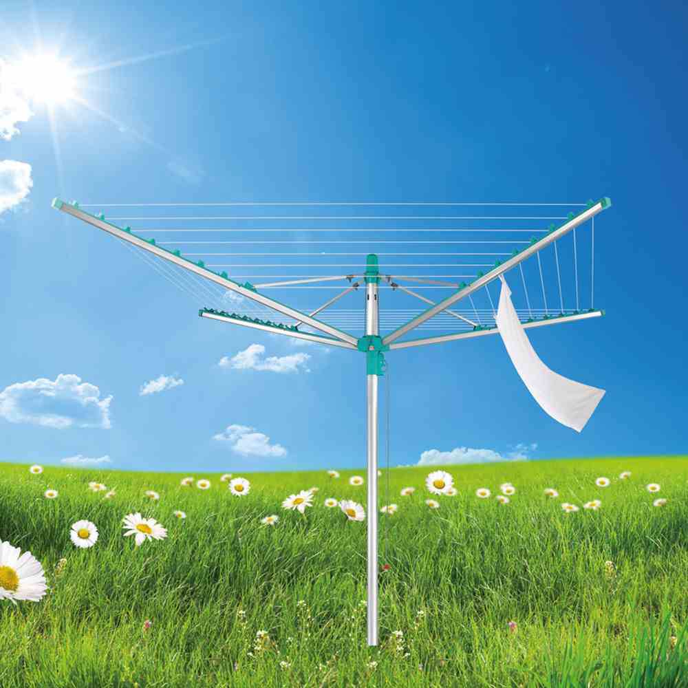 Een droogmolen in de buitenlucht met een wit katoenen doek opgehangen op een groene weide onder een heldere, zonnige hemel.