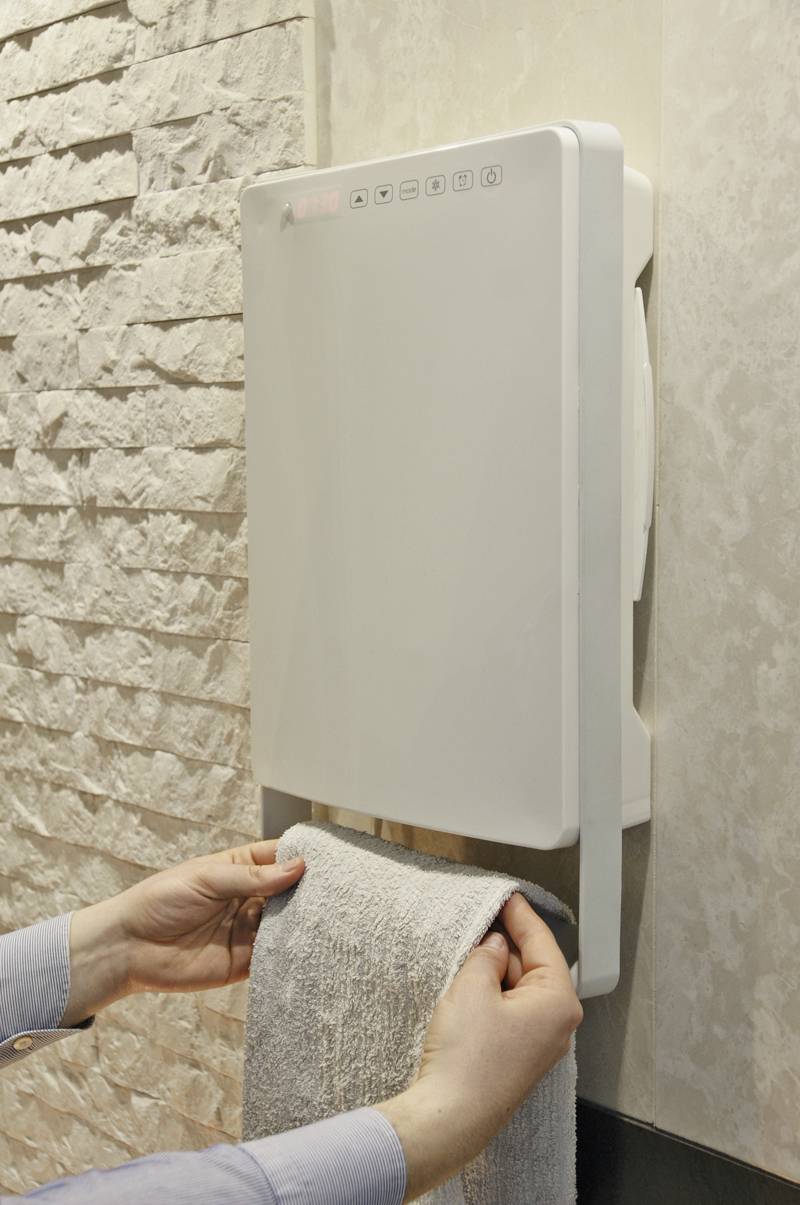 Een persoon droogt een handdoek aan een elektrische handdoekradiator die aan de muur is bevestigd in een badkamer.