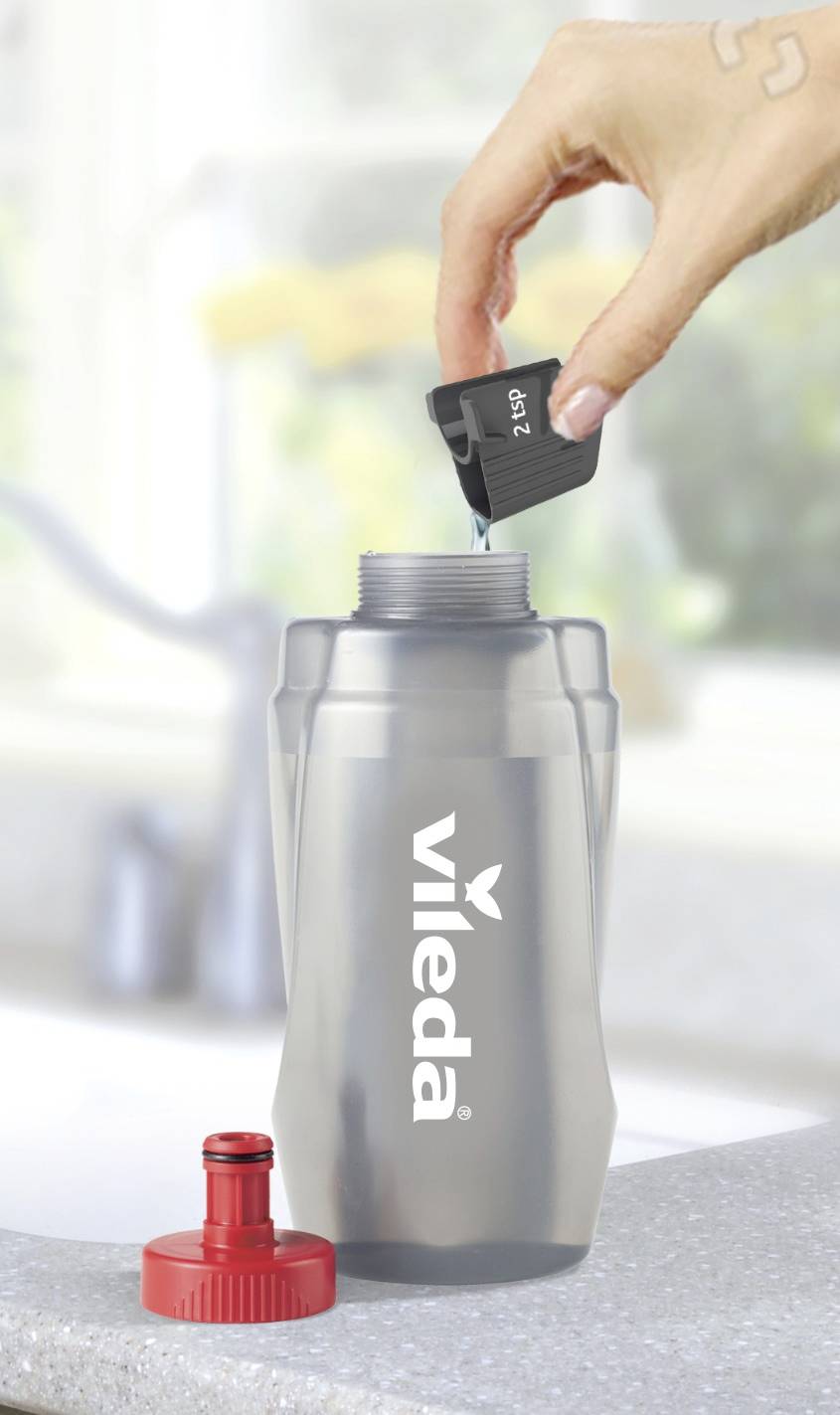 Een hand houdt een zwarte dop met het opschrift 'cat7' vast boven een transparente Vileda-fles op een aanrecht.