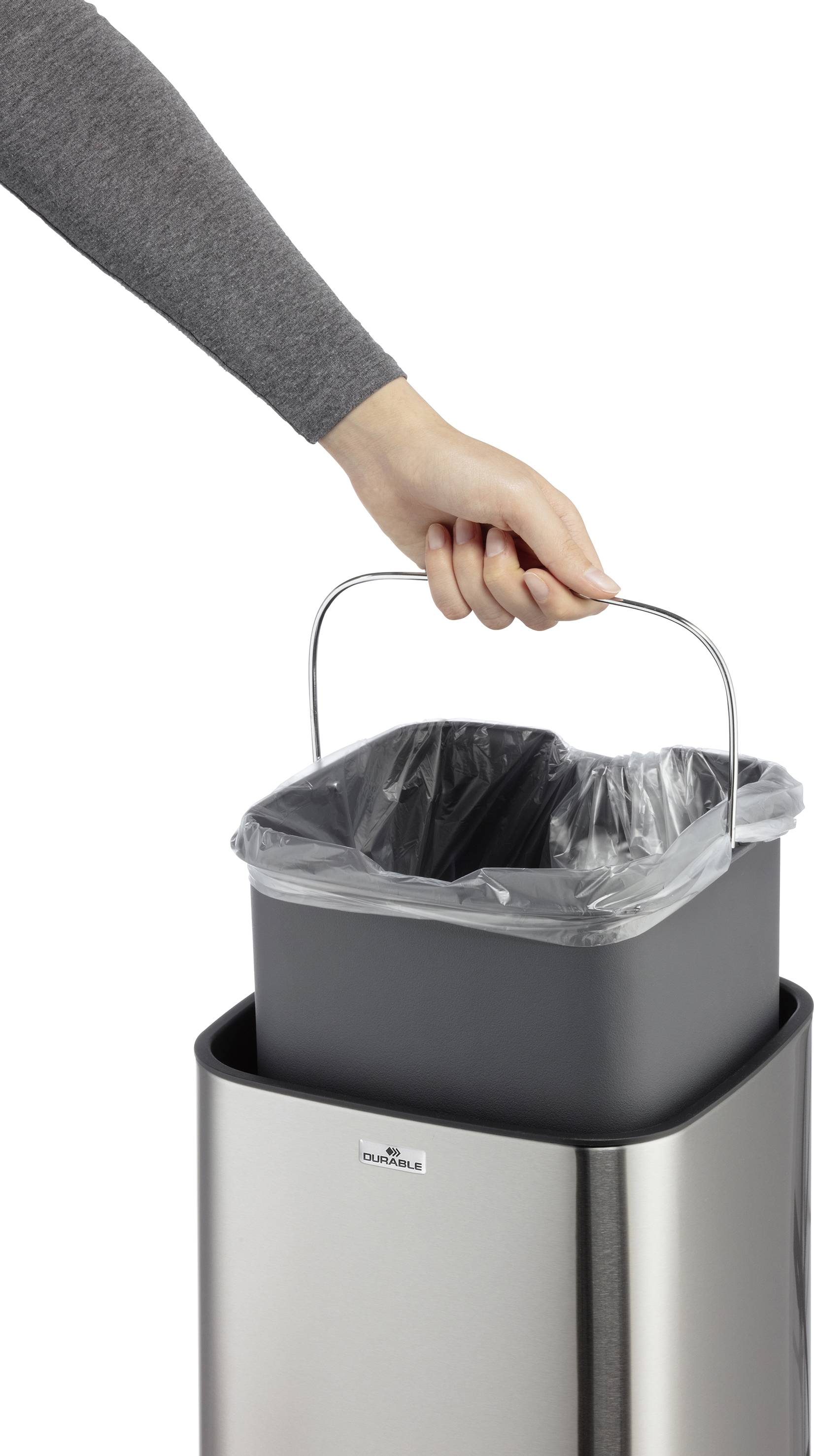 Een hand trekt een binnenemmer met vuilniszak uit een zilveren prullenbak.