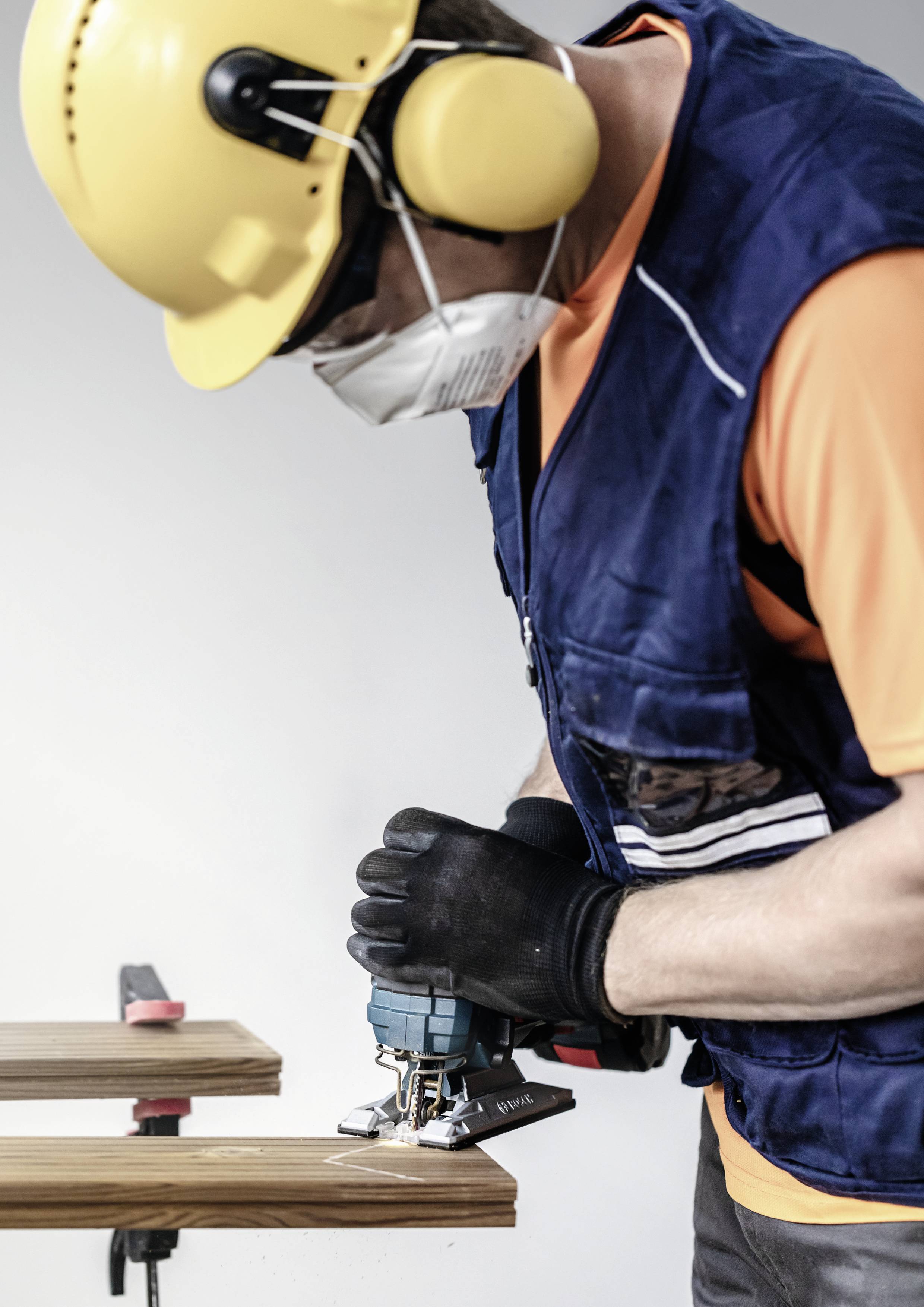 Een arbeider met helm, gehoorbescherming en masker zaagt hout met een elektrische zaag.