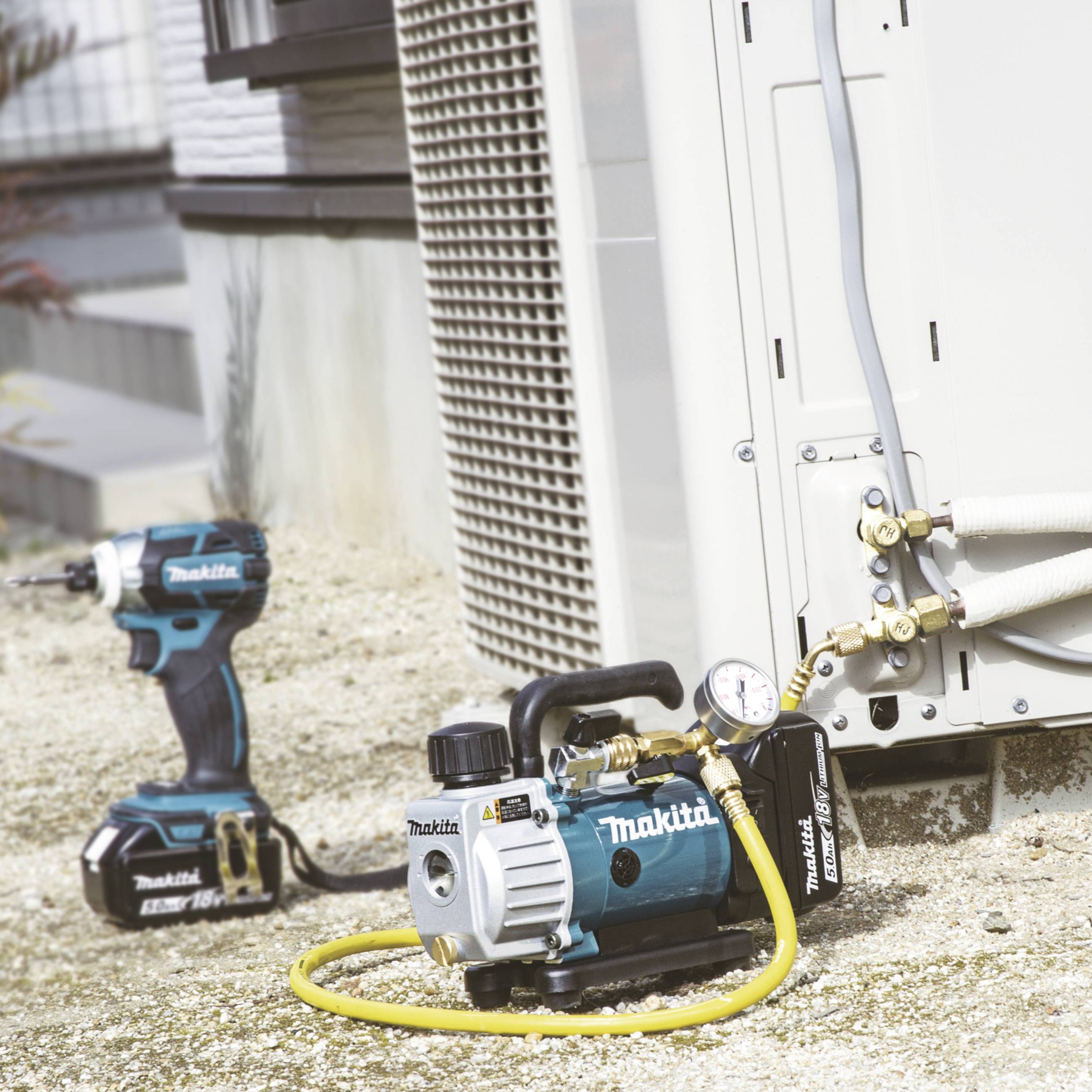 Een elektrische luchtpomp en een boormachine van Makita naast een buitenunit van een airconditioning.