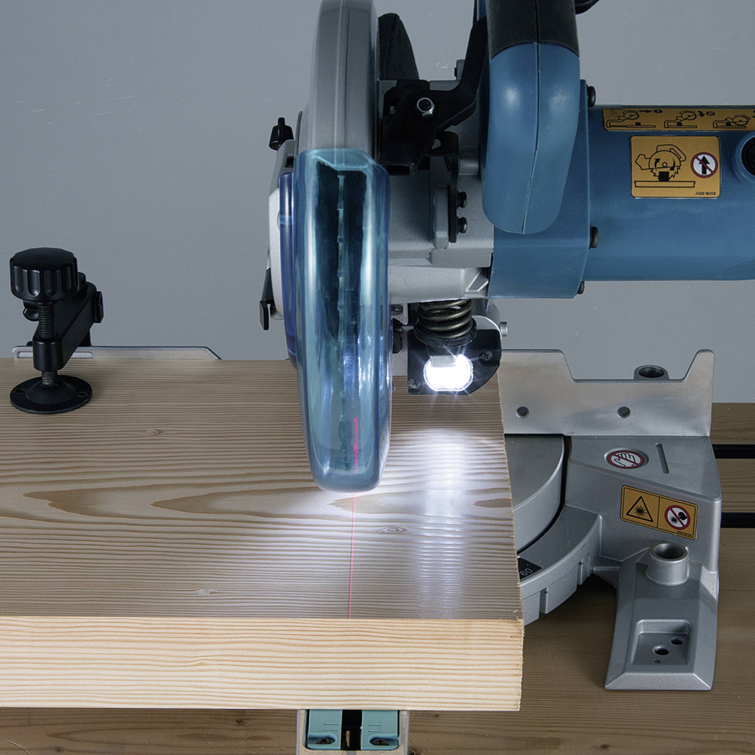 Cirkelzaag zaagt houten plank, rode laserstraal toont snijlijn. Veiligheidsvoorzieningen en waarschuwingssymbolen zichtbaar.