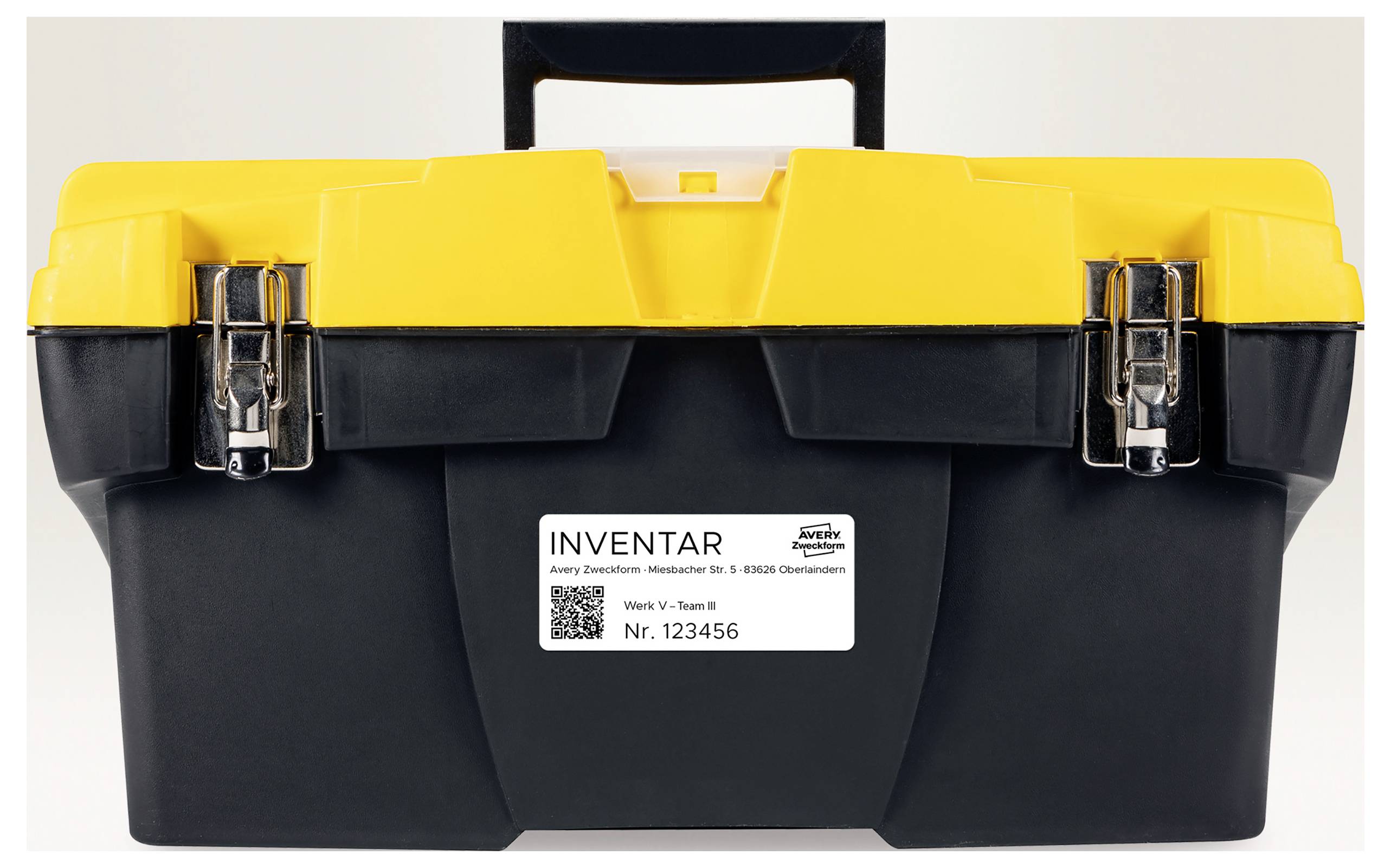 Zwarte gereedschapskist met geel deksel en draaggreep, aan de voorkant een inventariskaartje met barcode en nummer 'Nr. 123456'.