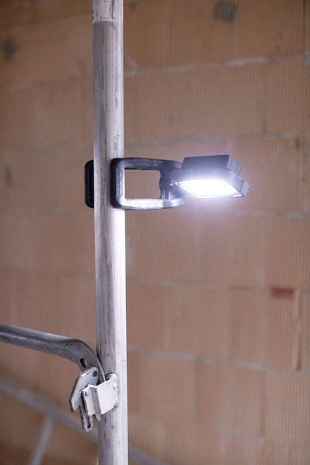 Een heldere lamp is bevestigd aan een metalen buis en schijnt. Op de achtergrond zijn onbepleisterde bakstenen te zien.