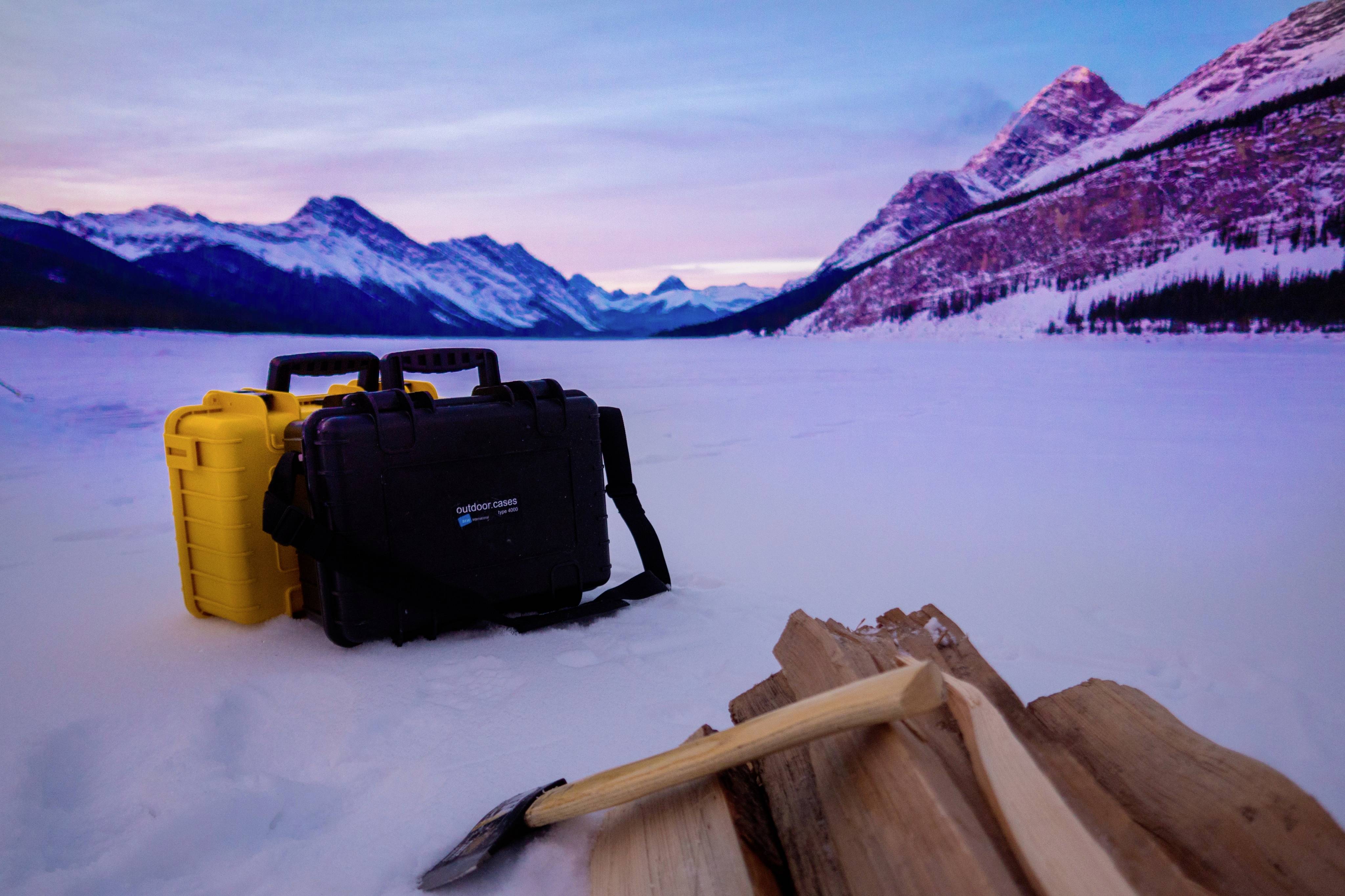 Uitzicht op een besneeuwde berglandschap bij schemering. Op de voorgrond liggen een bijl en brandhout, naast twee koffers.