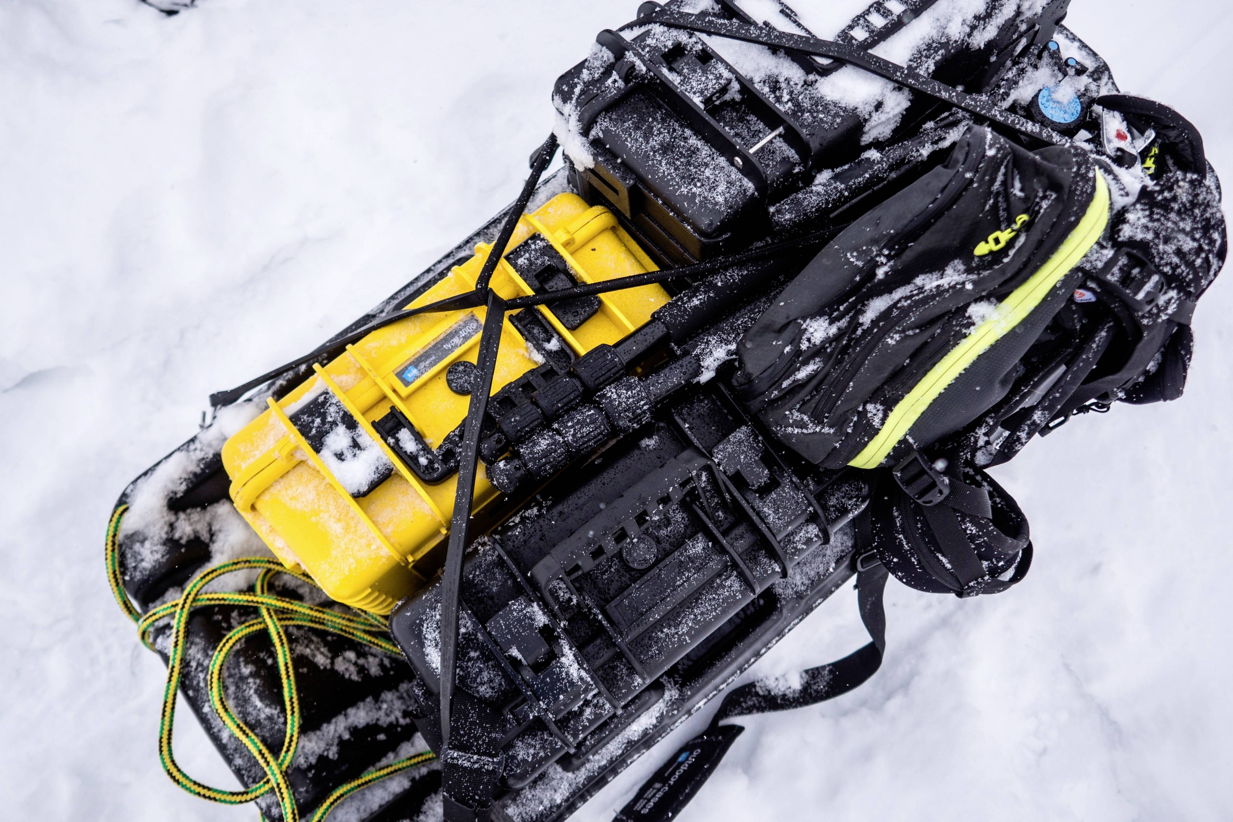Verpakte uitrusting op een slee in de sneeuw, bestaande uit gele en zwarte tassen, vastgemaakt met riemen, toont voorbereidingen voor expedities.