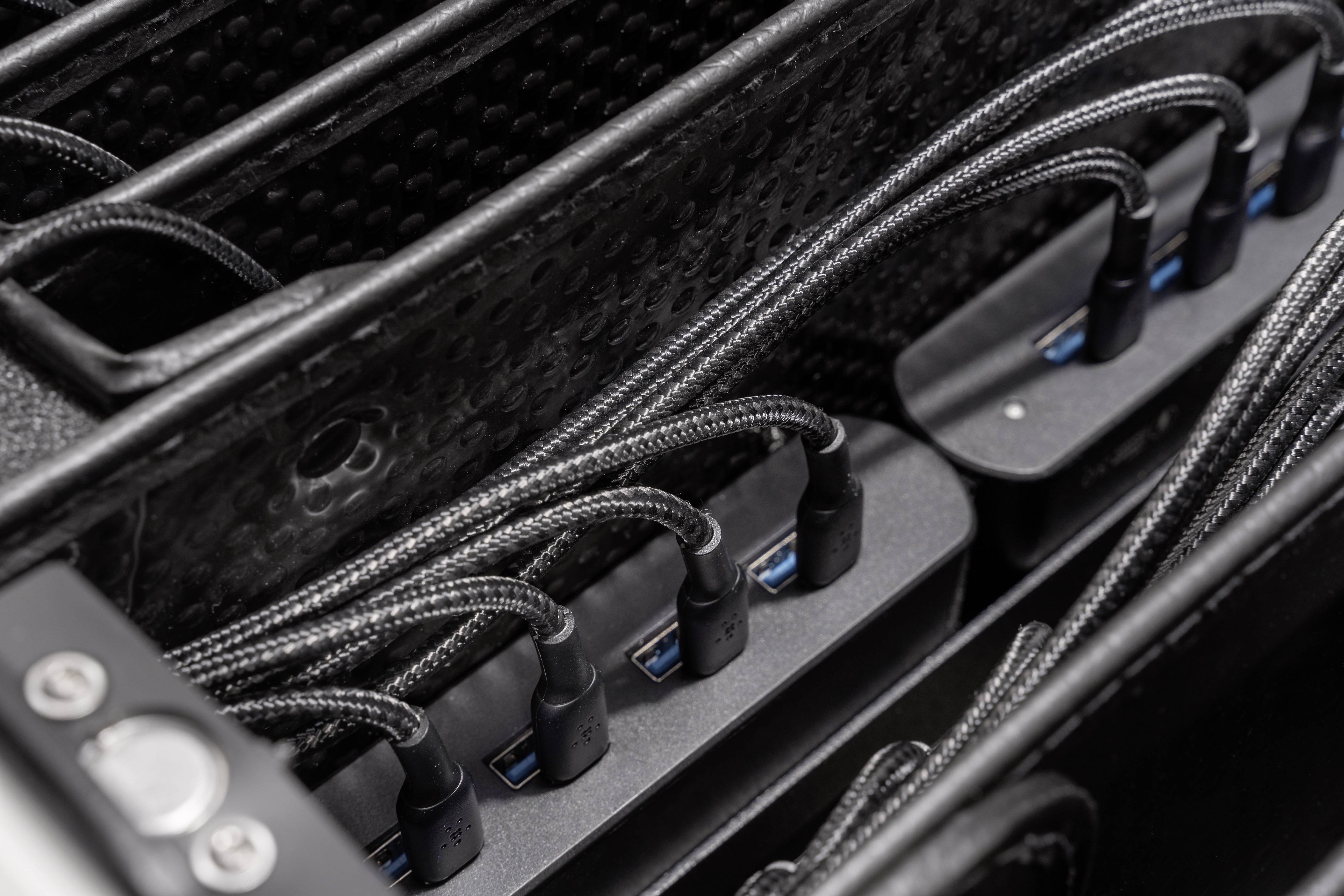 Verschillende zwarte USB-kabels zijn aangesloten op poorten van een laadeenheid die het frame van een oplaadsysteem laat zien.