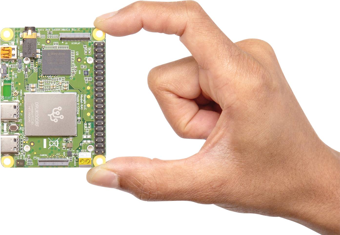 Een hand houdt een kleine groene printplaat vast met meerdere aansluitingen en een grote chip in het midden.