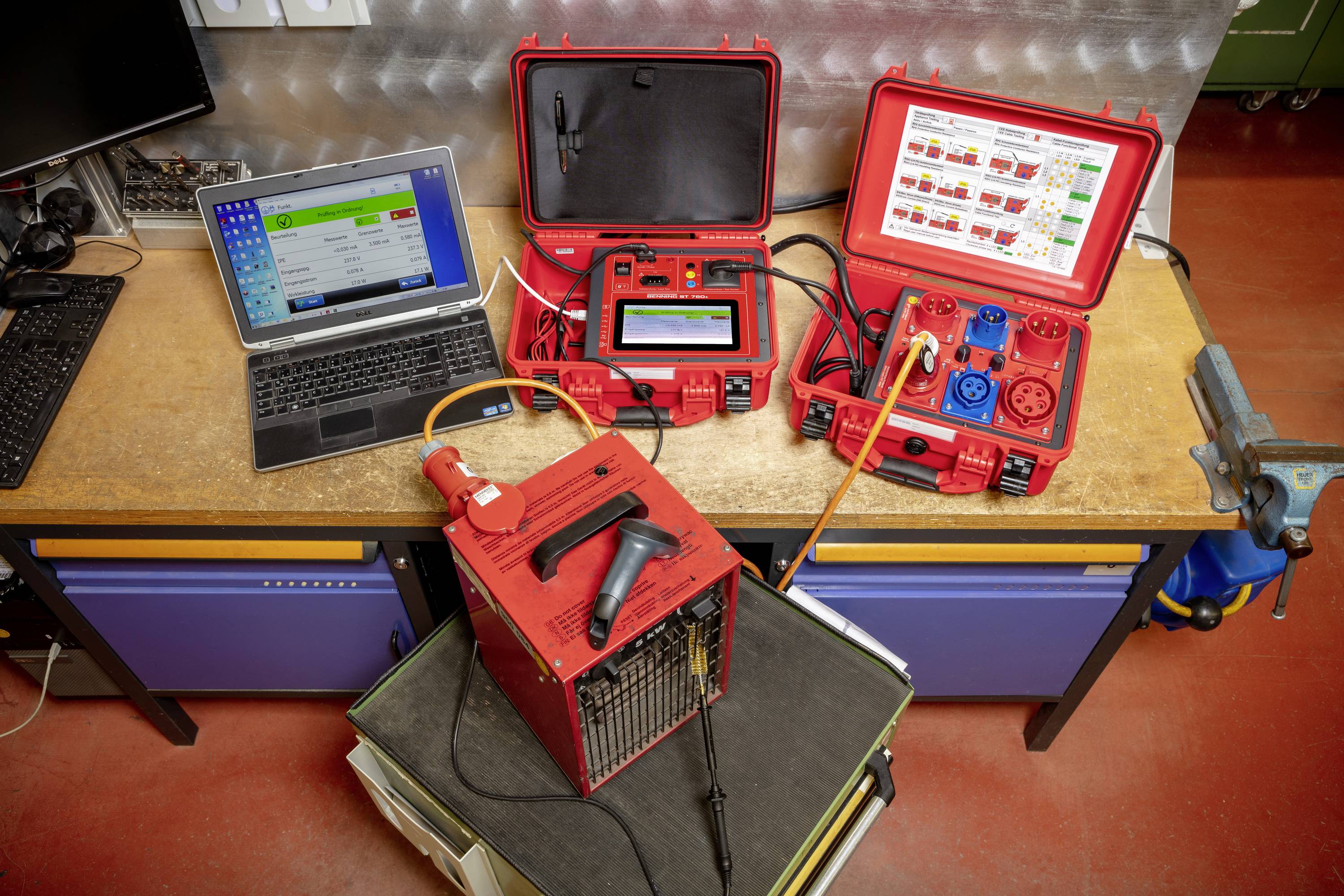 Twee rode koffers met technische apparatuur staan op een werkbank naast een laptop. Een apparaat test elektrische aansluitingen.