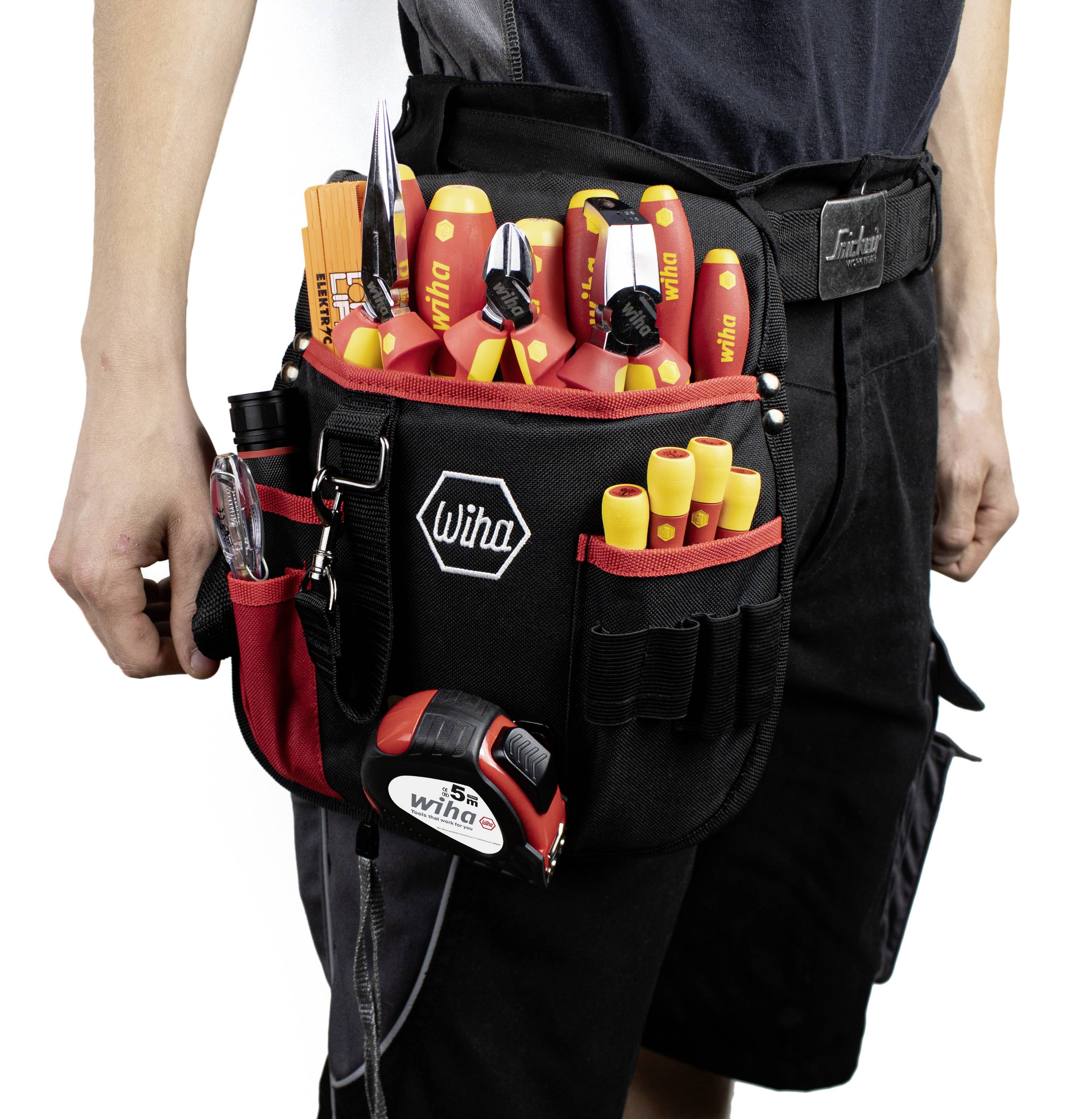 Een persoon draagt een gereedschapsriem met verschillende handgereedschappen en toebehoren. De riem heeft het 'Wiha'-logo en een rode tas.