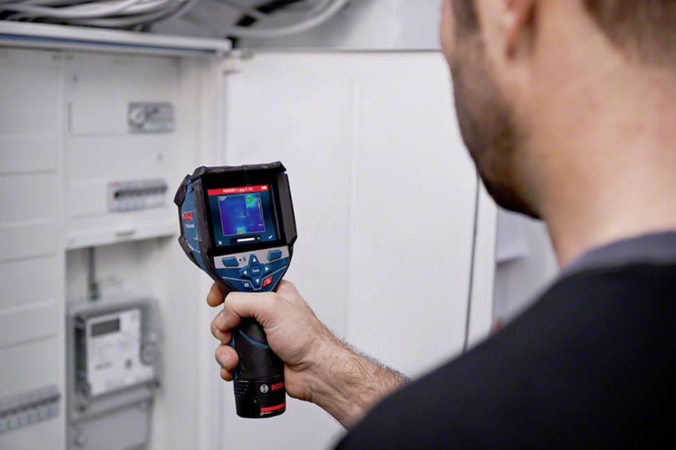Een persoon gebruikt een infrarood-thermometer om de temperatuur in een elektrische schakelkast te controleren.