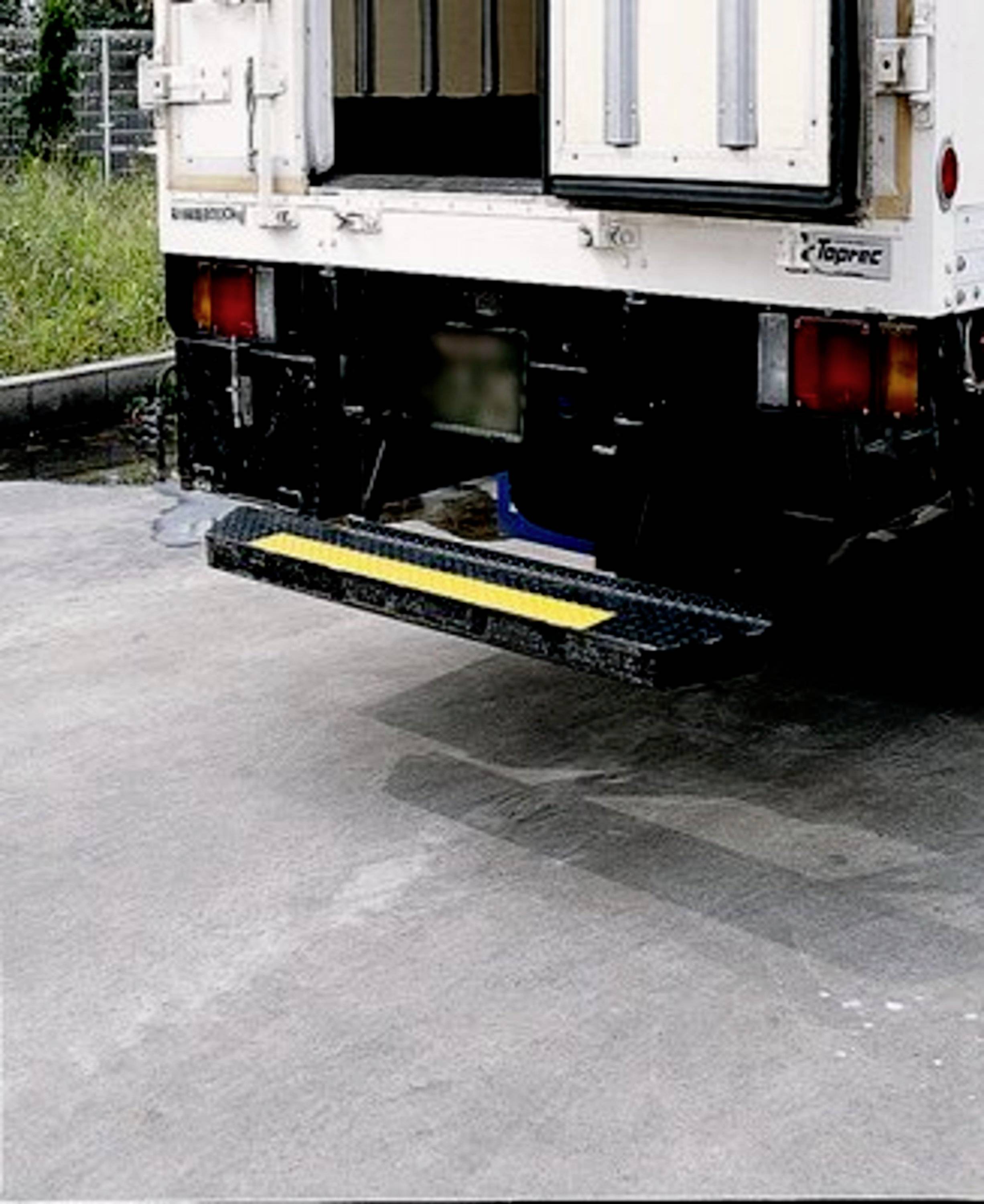 Achteraanzicht van een vrachtwagen met een open deur en uitgeschoven instaptrede op een industrieterrein.