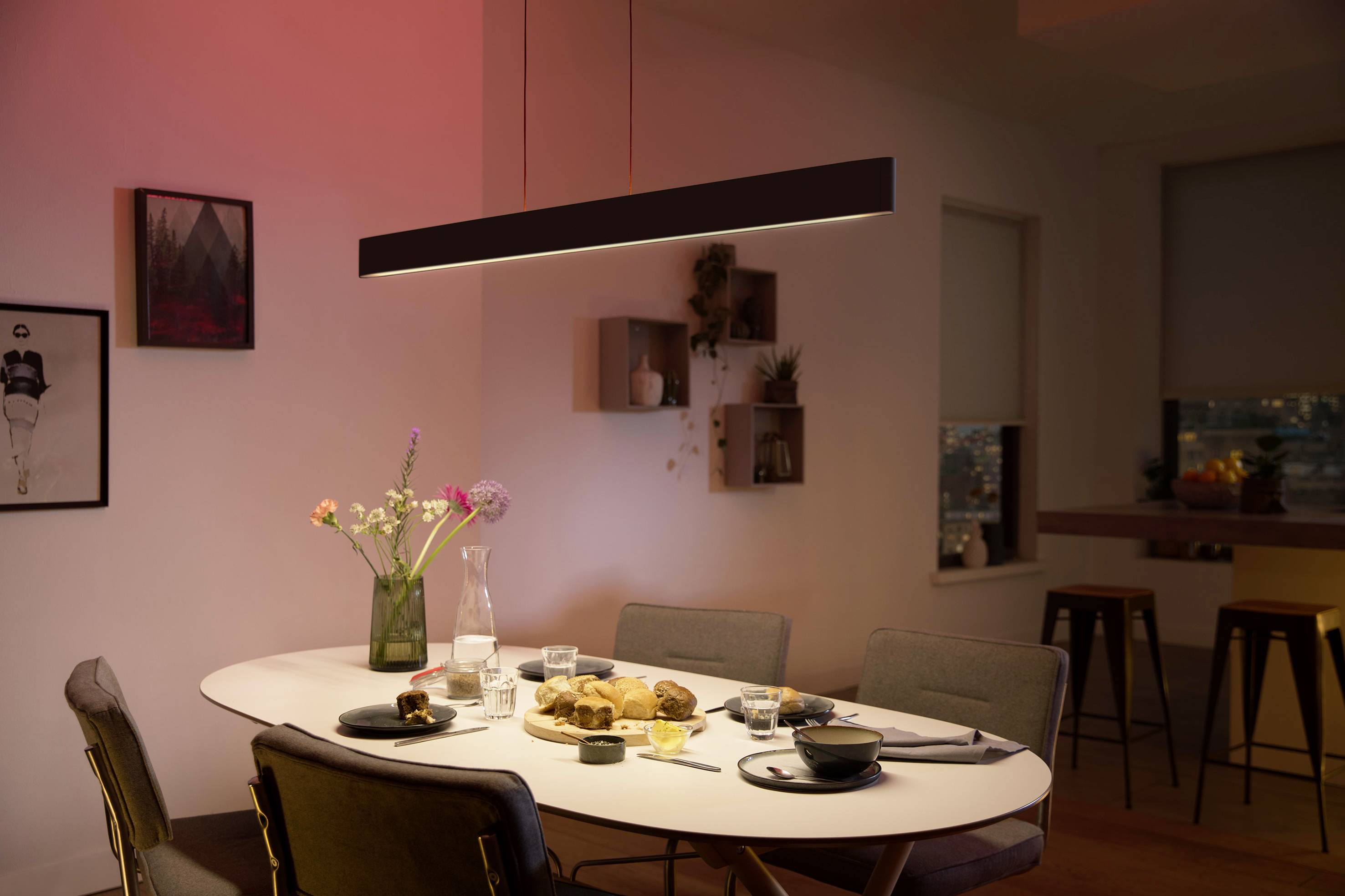 Eetkamer met tafel, stoelen en gedekte tafel. Een hanglamp verlicht de ruimte met rood licht. Wanddecoraties op de achtergrond.