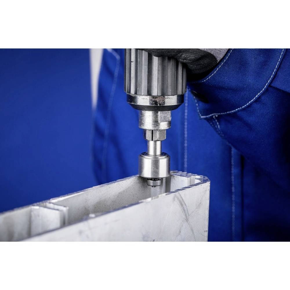 Een persoon boort met een metaalsnijder in een aluminiumprofiel. Hij draagt blauwe werkkleding. Hoofdfocus op de boor.