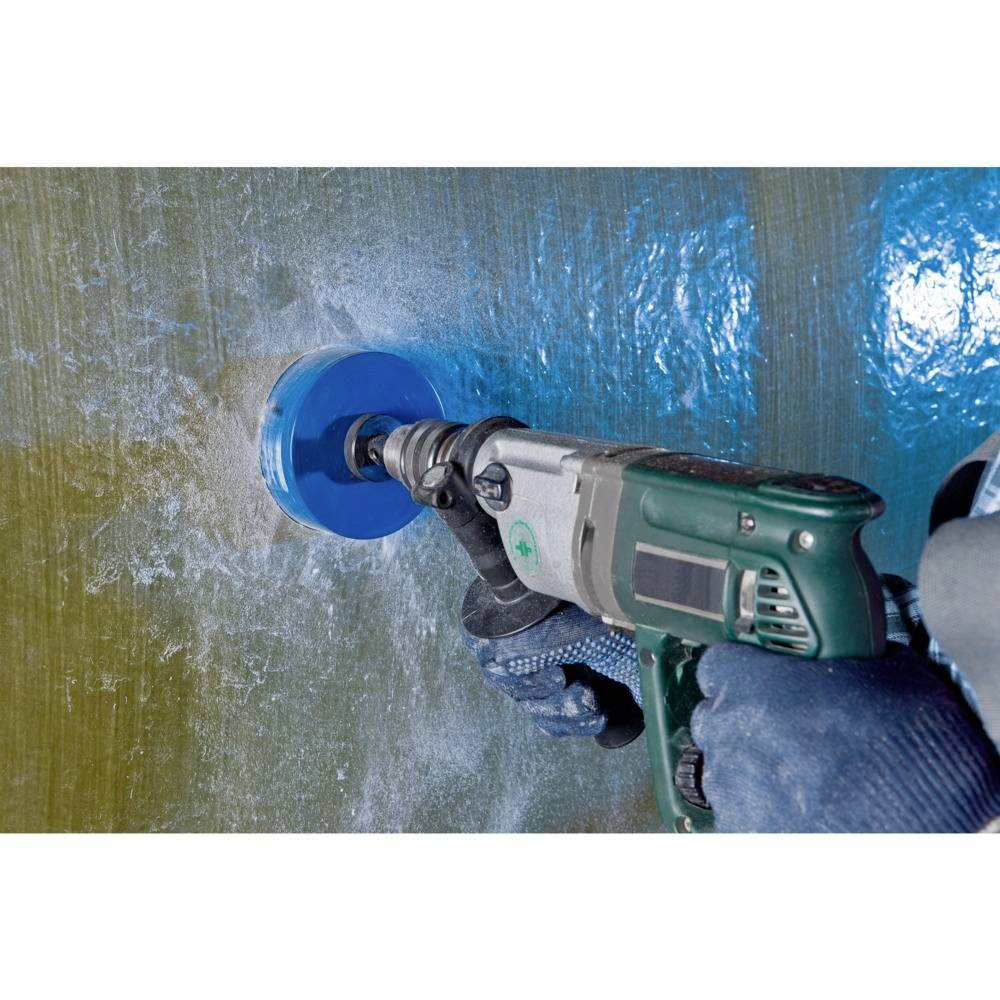 Een hand houdt een boormachine met een blauwe boorbit vast en boort in een glasvezelversterkt kunststofoppervlak.